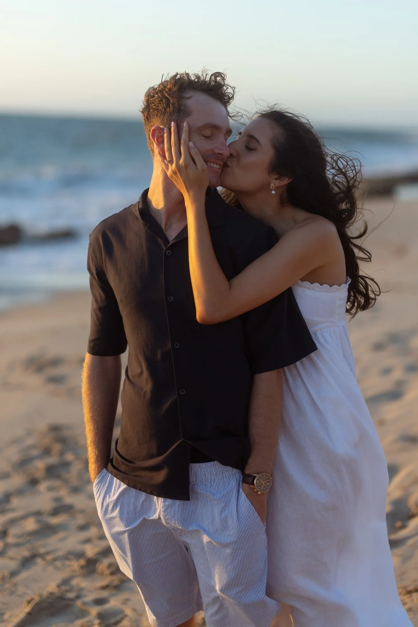 A couple share a tender sunset kiss on a windswept beach during their romantic pre-wedding shoot in Perth.