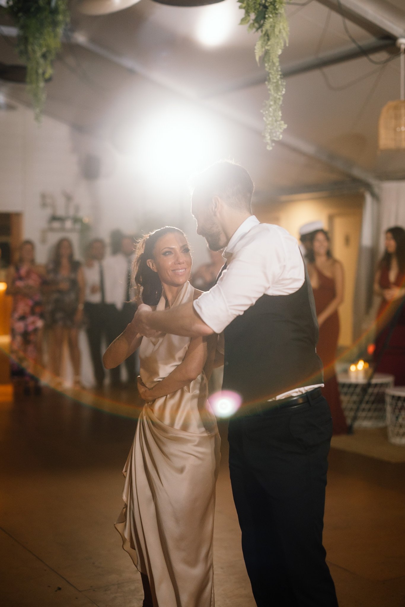 Romantic close portrait of a bride in a champagne silk gown dancing with her groom under hanging greenery and dramatic light flare at a Swan Valley wedding reception, photographed by James Di Stefano