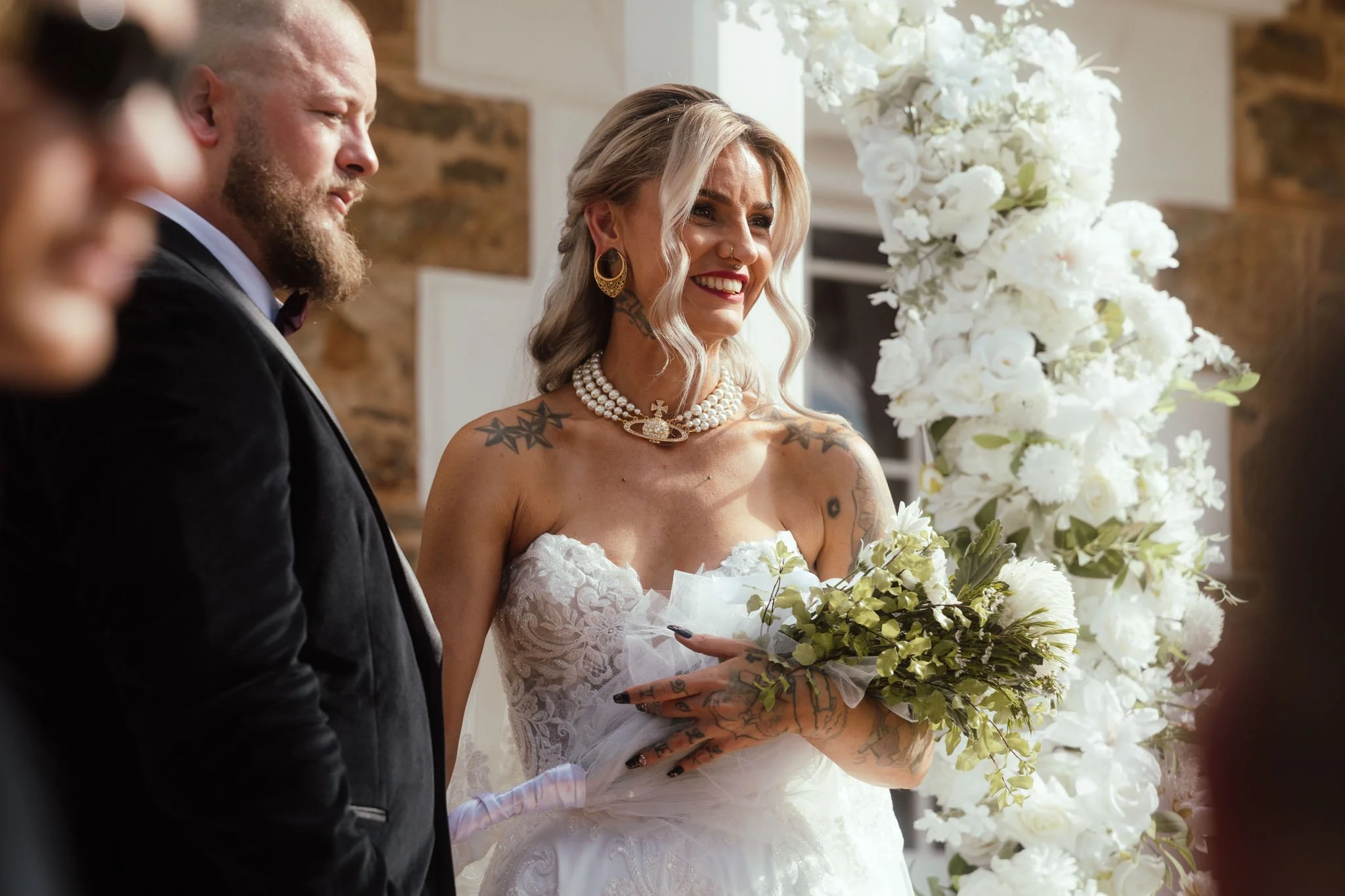 A close-up editorial portrait of the smiling bride at Buckland Estate, showcasing her elaborate pearl choker, ornate wedding dress bodice, and delicate green and white bouquet, captured by a luxury Perth wedding photographer.