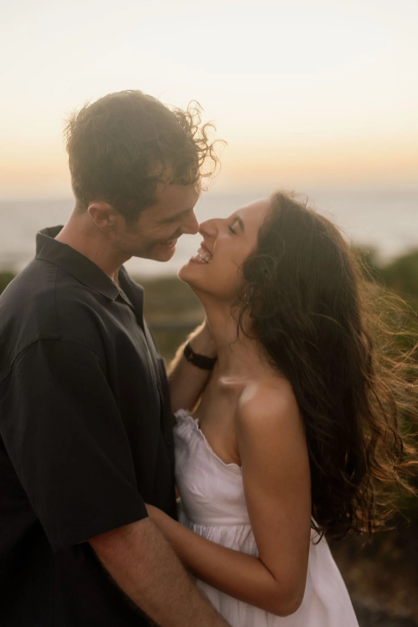 A couple share a joyful almost-kiss at golden hour during a cinematic pre-wedding shoot at Perry's Paddock, hair swept by the wind