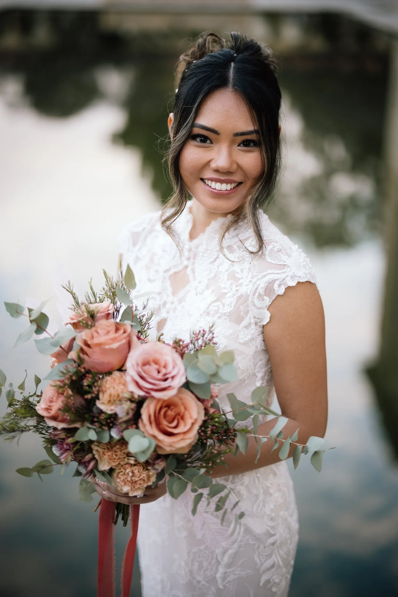 Bride in an off-shoulder satin gown with floral appliqué walks smiling as bridesmaids in burgundy carry her billowing train.