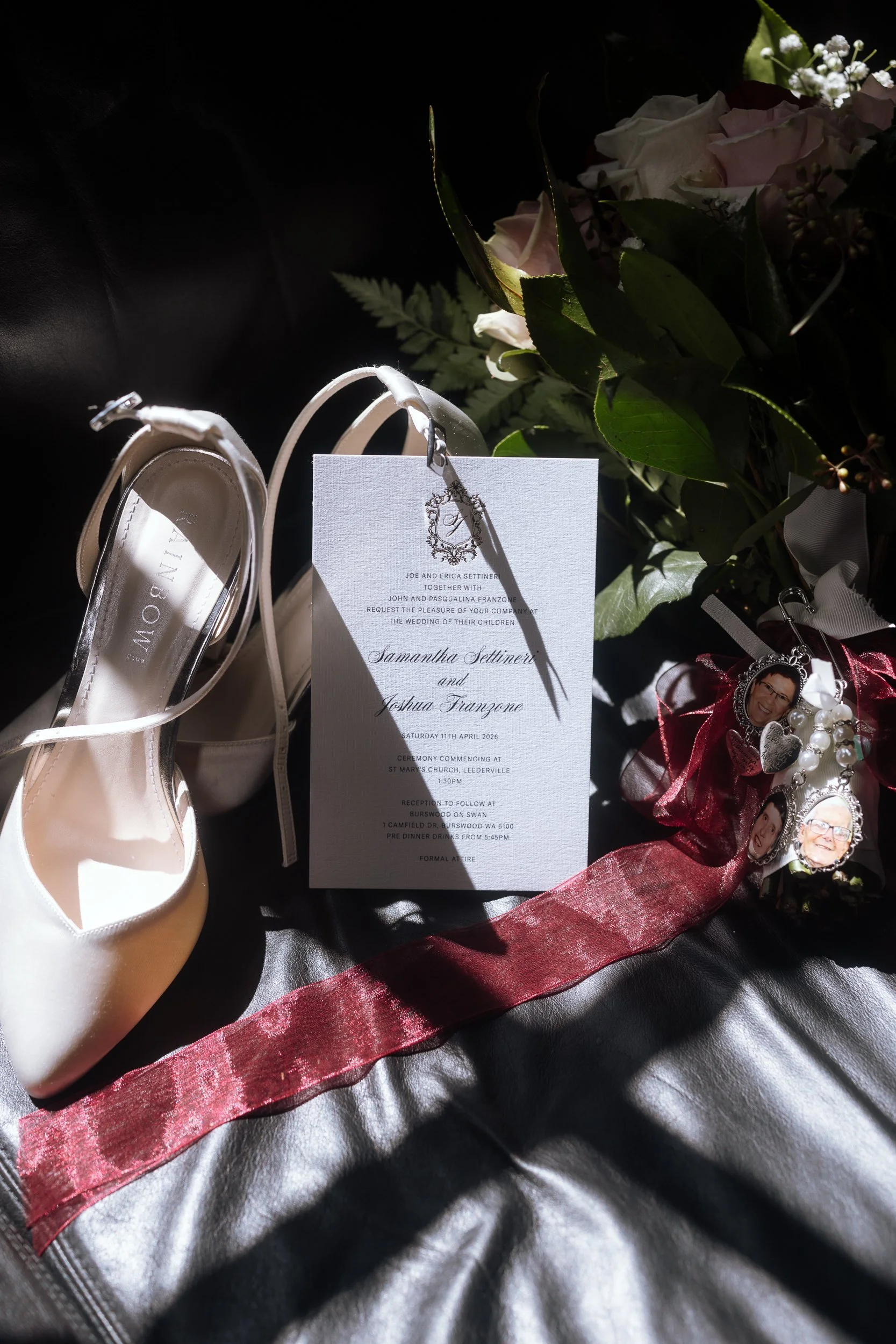 Elegant wedding flat lay featuring a calligraphy invitation, ivory heels, blush bouquet, and photo memorial charms tied