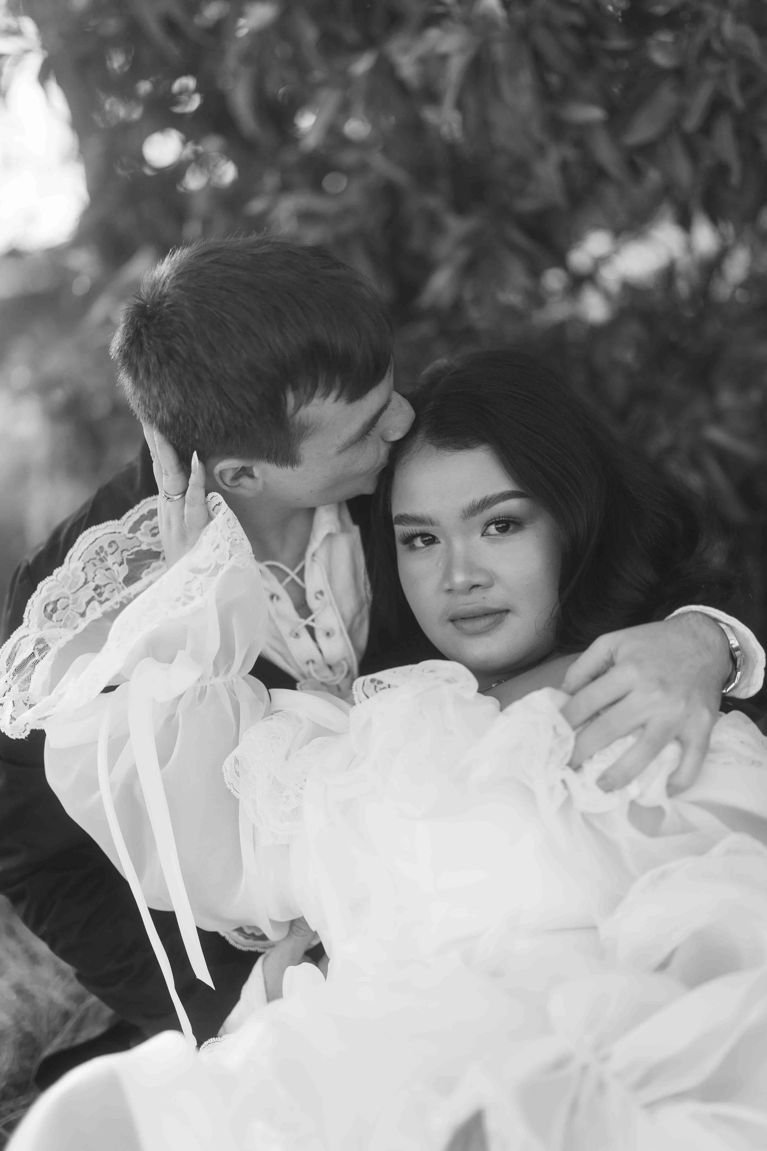 Groom tenderly kisses his bride's temple as she gazes forward, her ruffled lace gown catching soft light at Perry's Paddock.