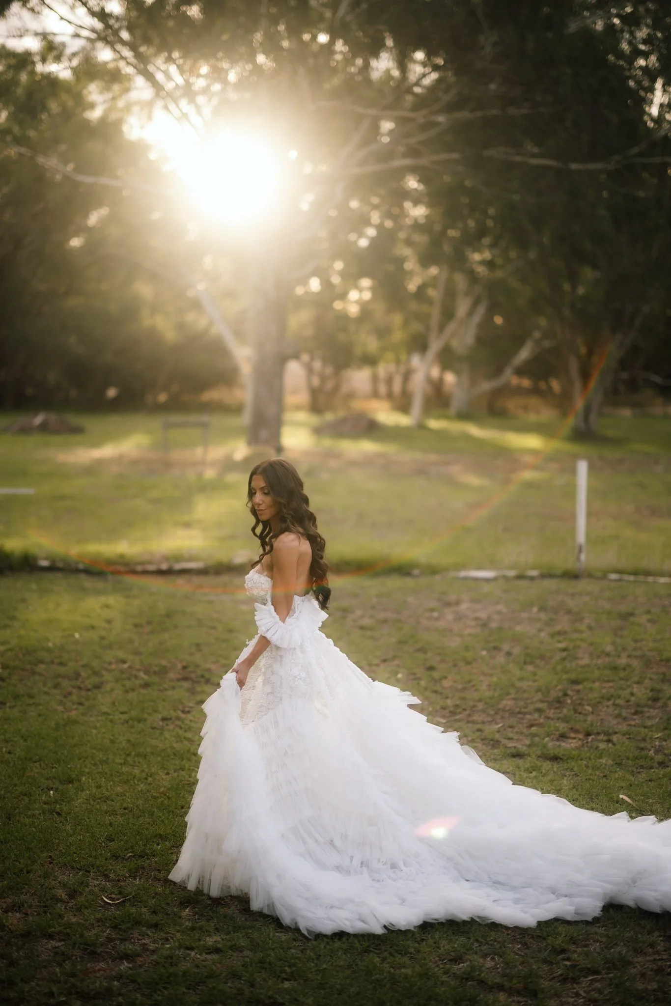 Bride in a dramatic ruffled tulle gown with a long cathedral train standing in golden sunset light among native trees at The Mallard Duck Swan Valley, photographed by James Di Stefano