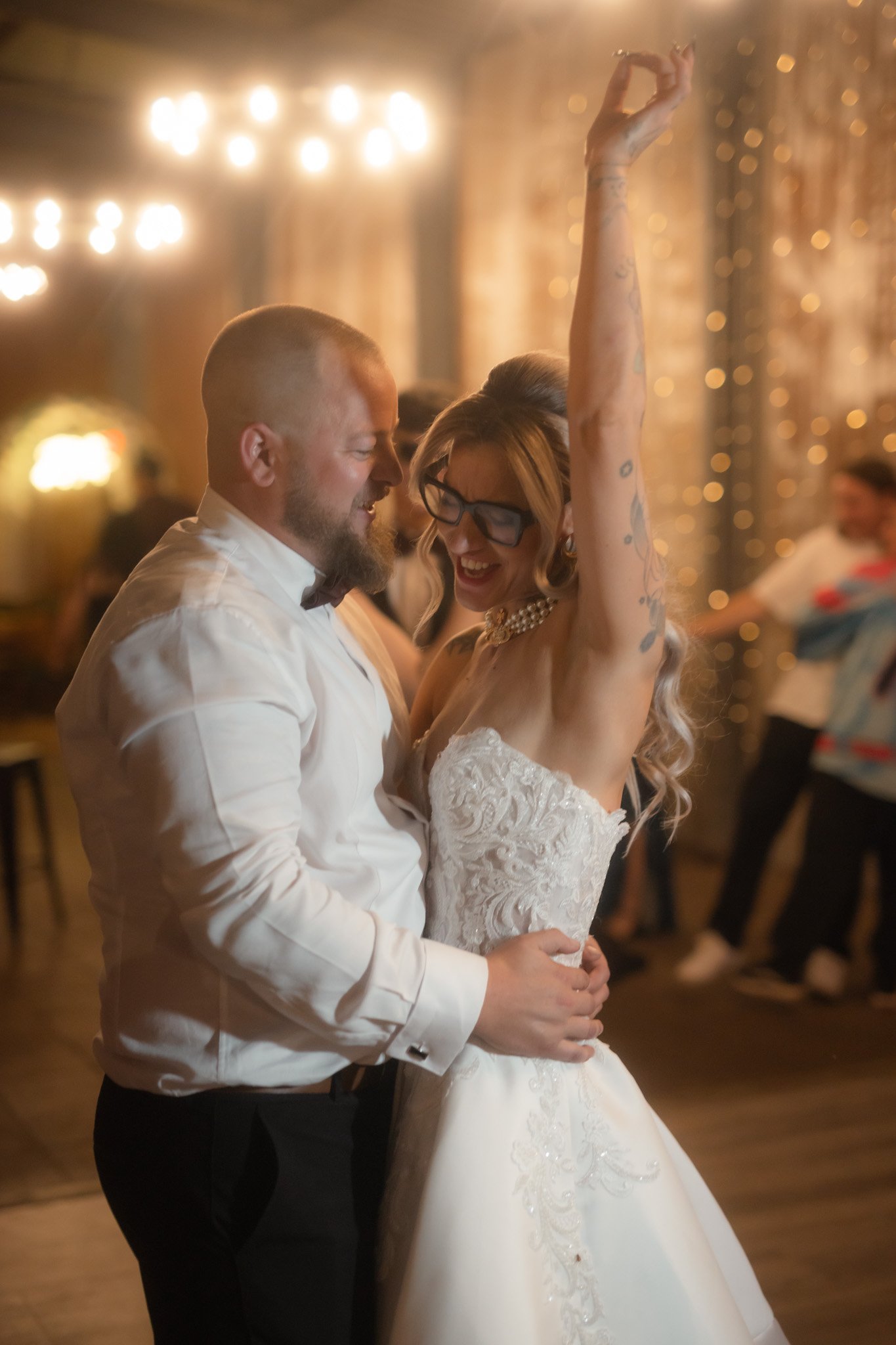 A joyful, candid photograph of the bride wearing stylish black glasses laughing with her hand raised in the air as she dances with her groom during their Buckland Estate barn reception