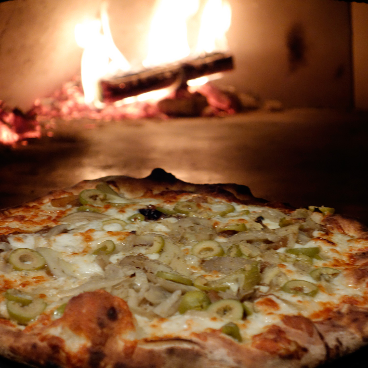 Fennel & Green Olive Pizza coming out of the wood oven