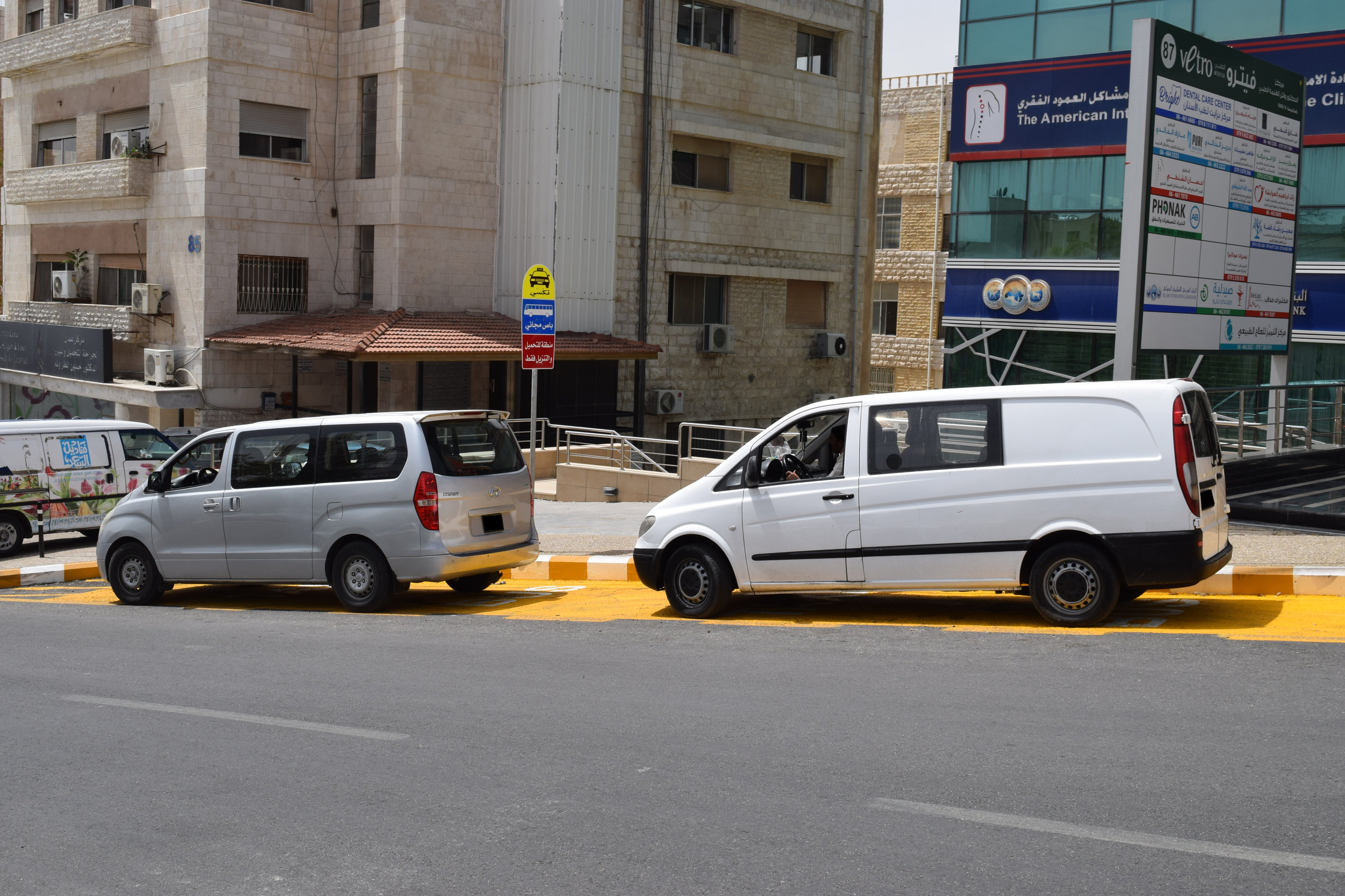  Two vans parked in a taxi parking zone. 