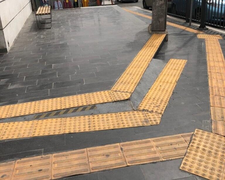  Ramped tactile navigational strips and metal sheet strips connecting the sidewalk to a building entrance. Note that the strips are applied in a rather haphazard manner. 