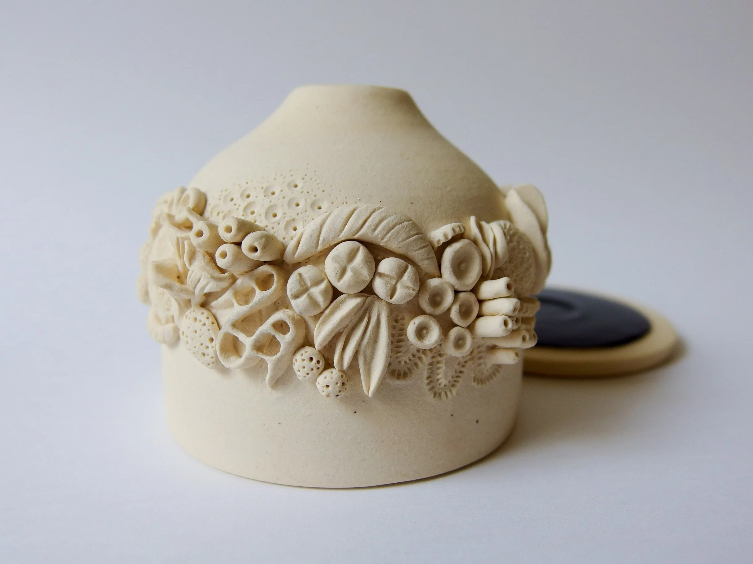 An off-white ceramic incense burner with intricate organic details on the exterior. The base sits behind it.