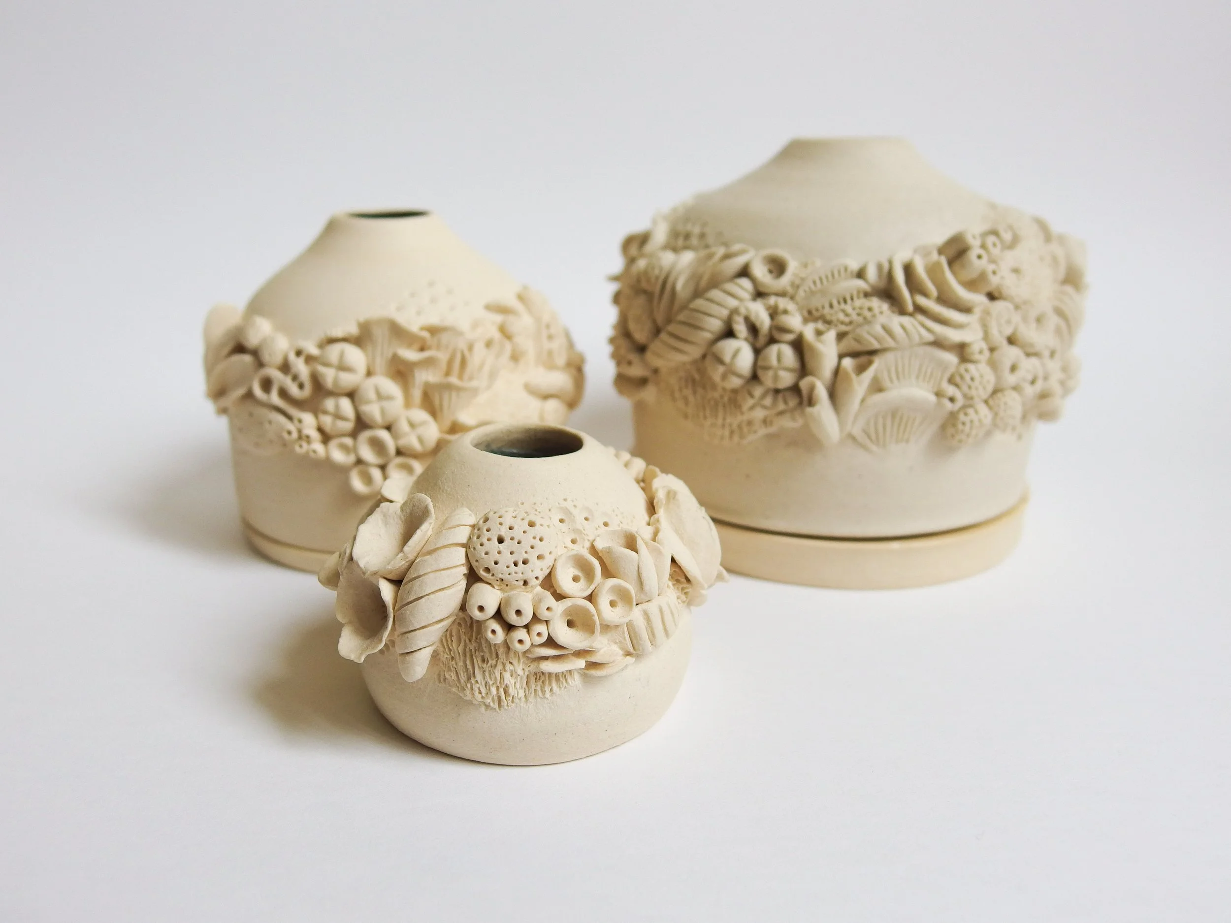 A set of three off-white ceramic incense burner with intricate organic details on the exterior