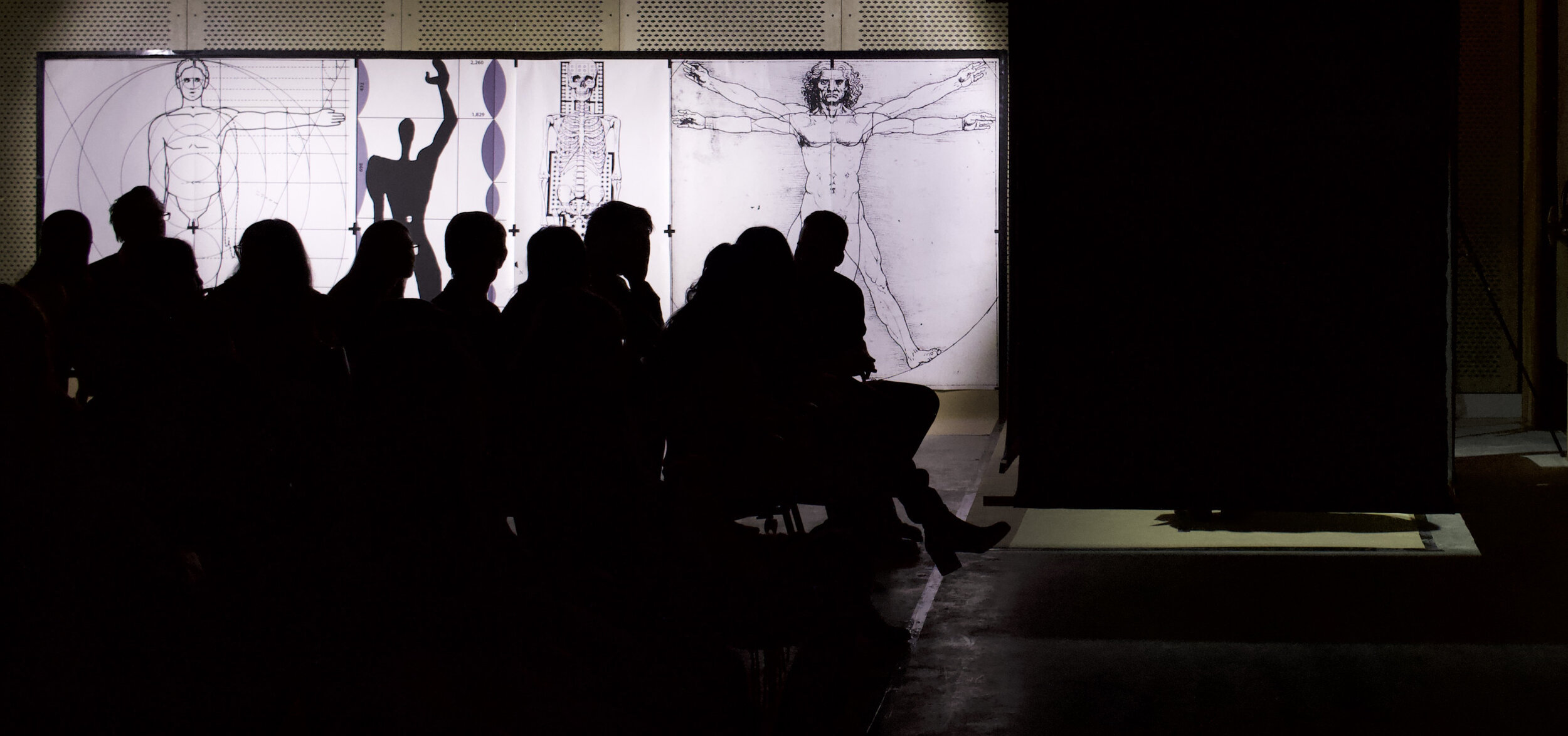  The scene of the performance mere moments before it began. While audience members glance around the room, a square of light can be seen beneath the black box housing the authors. Moments later, paint would spill from the box and go largely unnoticed