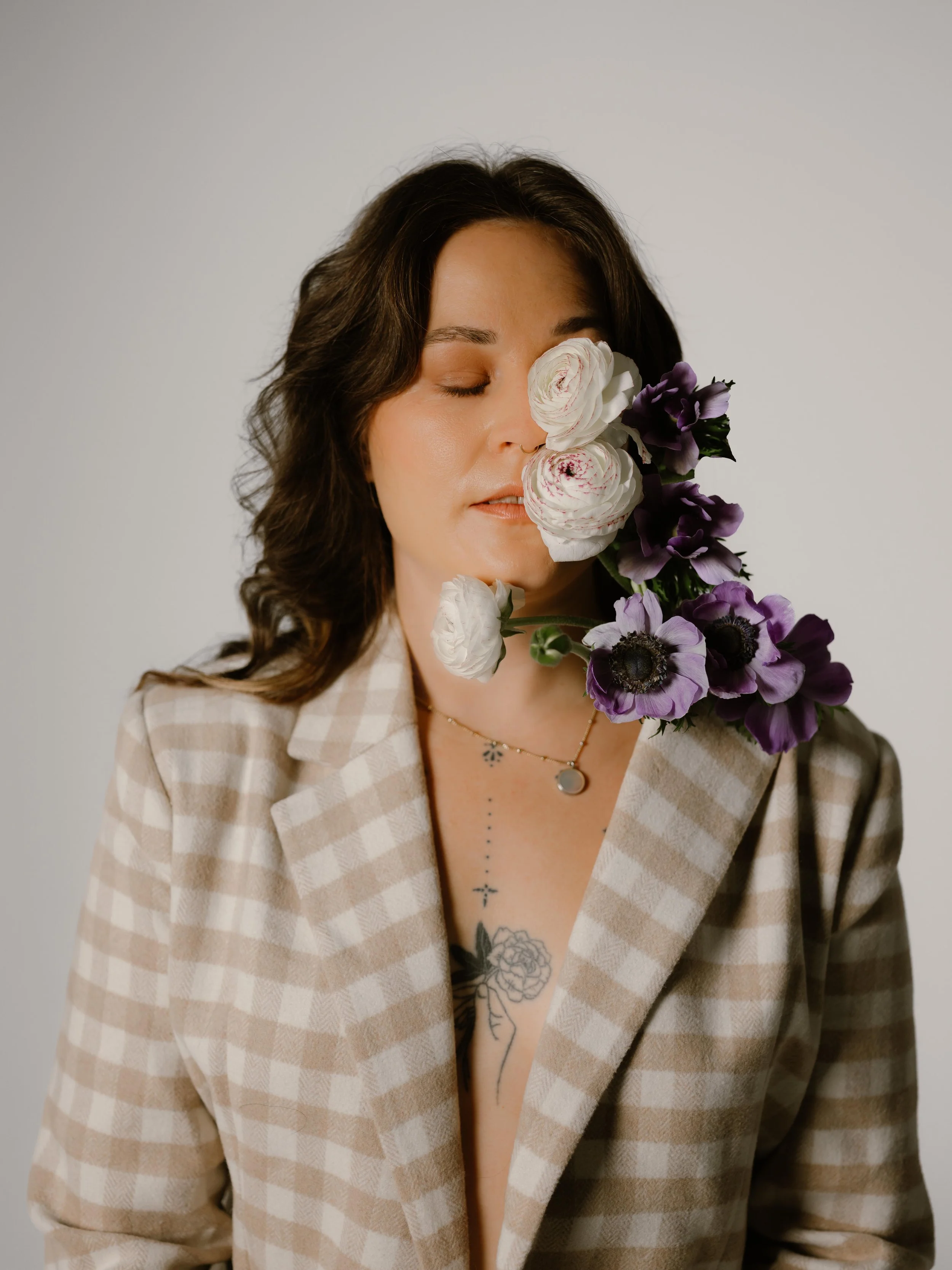 Photo of a woman wearing tan checkered blazer with purple and white flowers covering part of her face in a photo studio in seattle washington