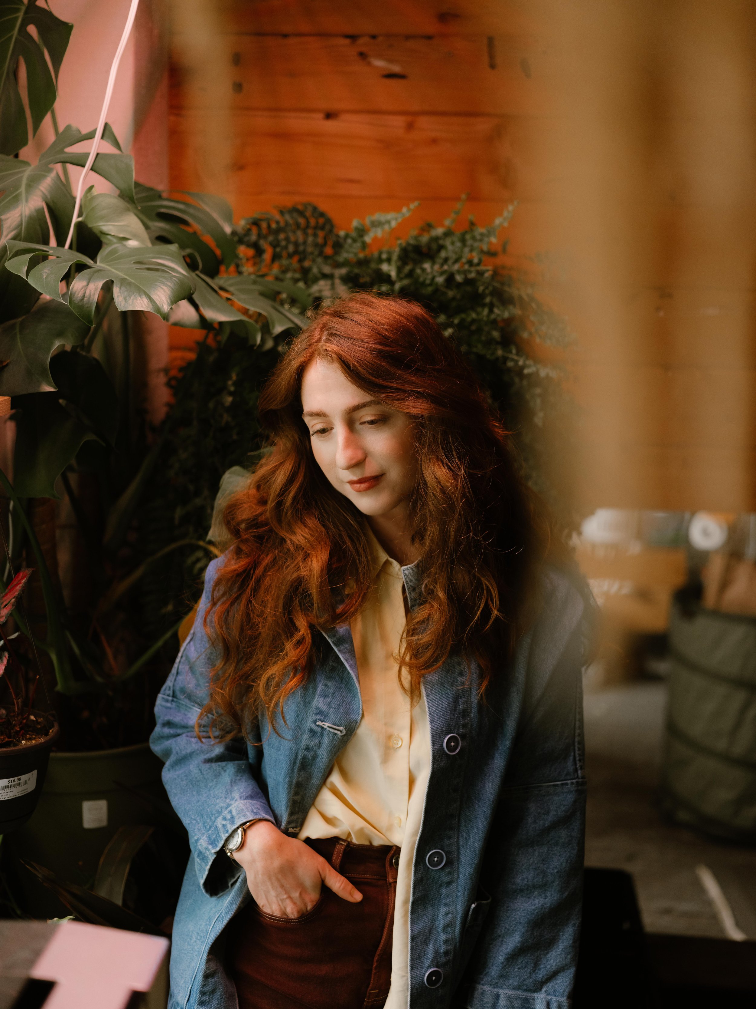 red haired woman standing in front of window surrounded by florals