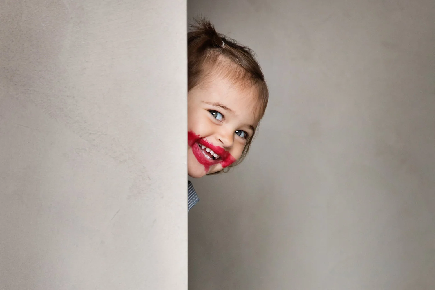 Smiling toddler with messy lipstick face by kids advertising photographer Lisa Tichané