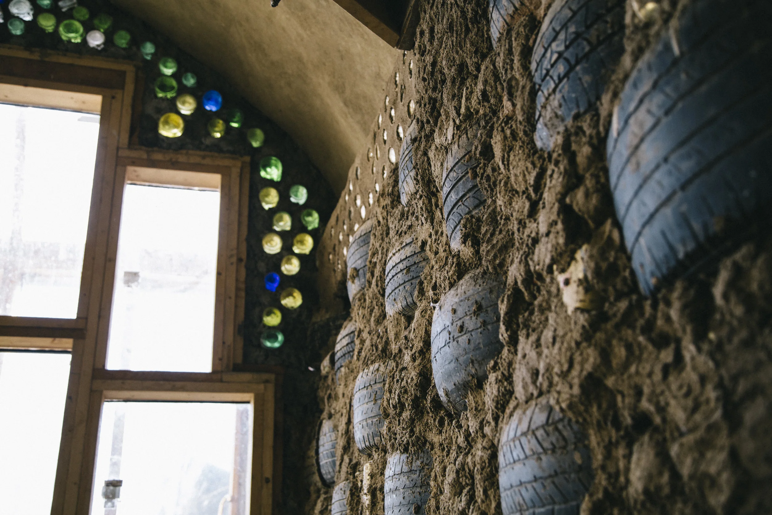 A wall made up of rammed-earth tires, and the colored jewels of light passing through bottle bricks.