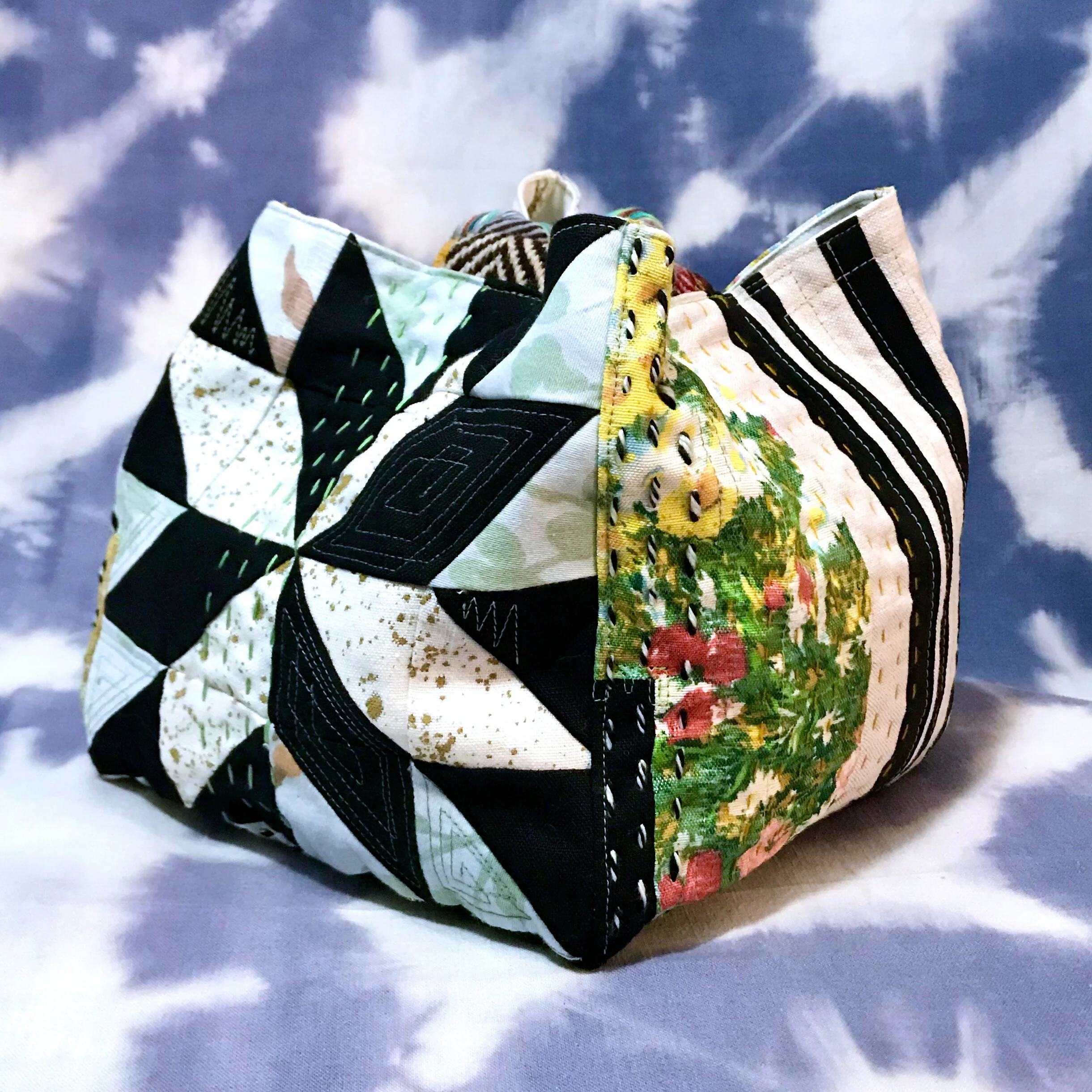 This modern komebukro inspired cinch sack features a patchwork of colors & textures on each of its 5 faces using a combination of machine & hand stitched quilting methods in high contrast black, white, natural flax, hand dyed, & floral print fabrics.