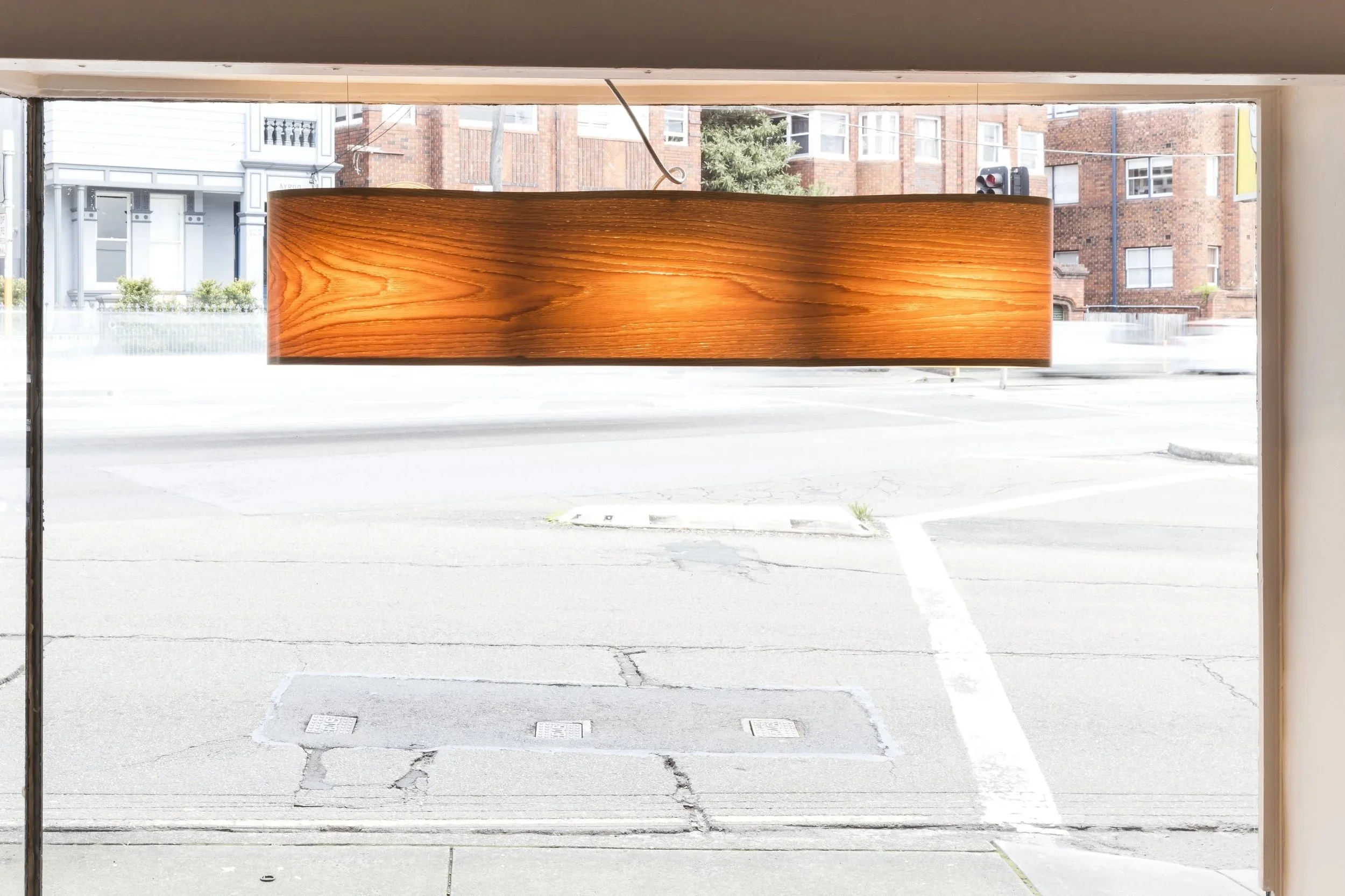 James Russ Infinity pendant. A beautiful wooden light fixture hanging in front of a large window, illuminating the wood grain.