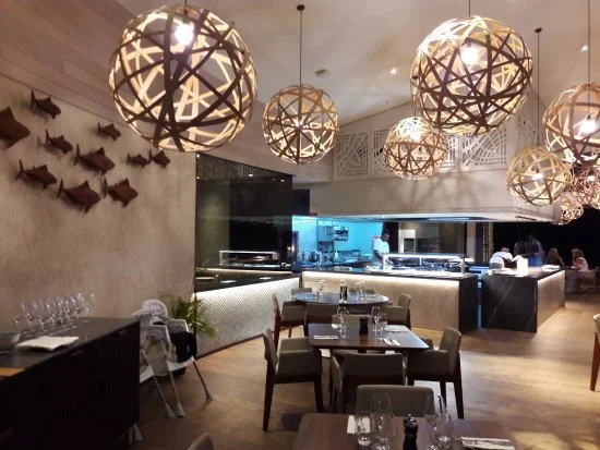 Elegant restaurant interior with hanging spherical light fixtures, fish wall decorations, and a modern open kitchen in the background.