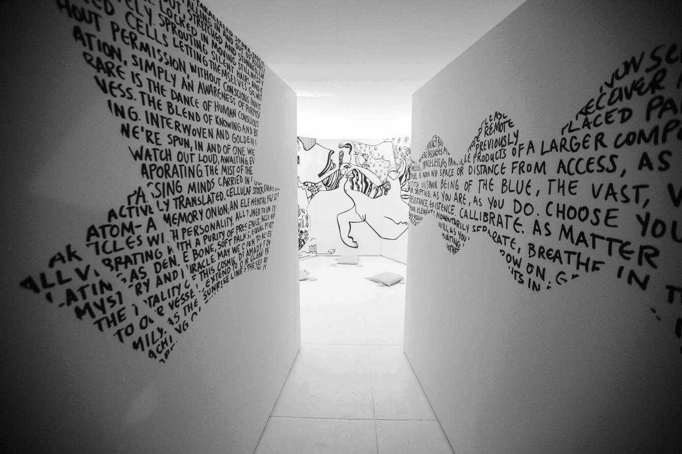 A conceptual installation that brings viewers into a state of presence to really absorb a piece of art rather than simply viewing and passing it by. My work has an intricate narrative and blossoms with time spent observing. I wanted to create a piece of work that you could leave your shoes and all the things you carried with you at the door, to enter into the art and its message, sit down and wander throughout its lines and create your own story through observation. It starts with a long narrowing hallway with stream of consciousness poetry hand painted on either wall; the left side has words encased in a geometric shape, representing the left (rational/logical) brain, and the right wall, the words are encased in a wave form shape to represent the flowing and more watery nature of the right brain. Walking in, your left and right hemispheres are soothed by the familiar, to be able to enter the space feeling tuned in. And walking out, balanced by the exposure to the polar opposite, preparing you to reenter the world feeling whole. The poems are intentionally fractured in moments due to the way they were created, some pieces of the message lost in the process. They also have neither a beginning nor end. These characteristics of the poems represent the stream-of-consciousness process, where producing within a flow state creates work that is able to capture only so much at one time. I liken it to sifting stones from sand, or cupping the hands to capture a drink of water; because I am influenced by the infinite nature of things, I am aware that whatever I am able to grab when I reach out into a vast well of ideas, is simply an observation on that present moment, and therefore, a truth worth observing. This said, my philosophy is based on valuing the act of reaching over controlling the outcome or producing something premeditated. My work is a vehicle to inspire others to do this kind of reaching inward and exploring, without judgment, to see and really treasure what we can discover.