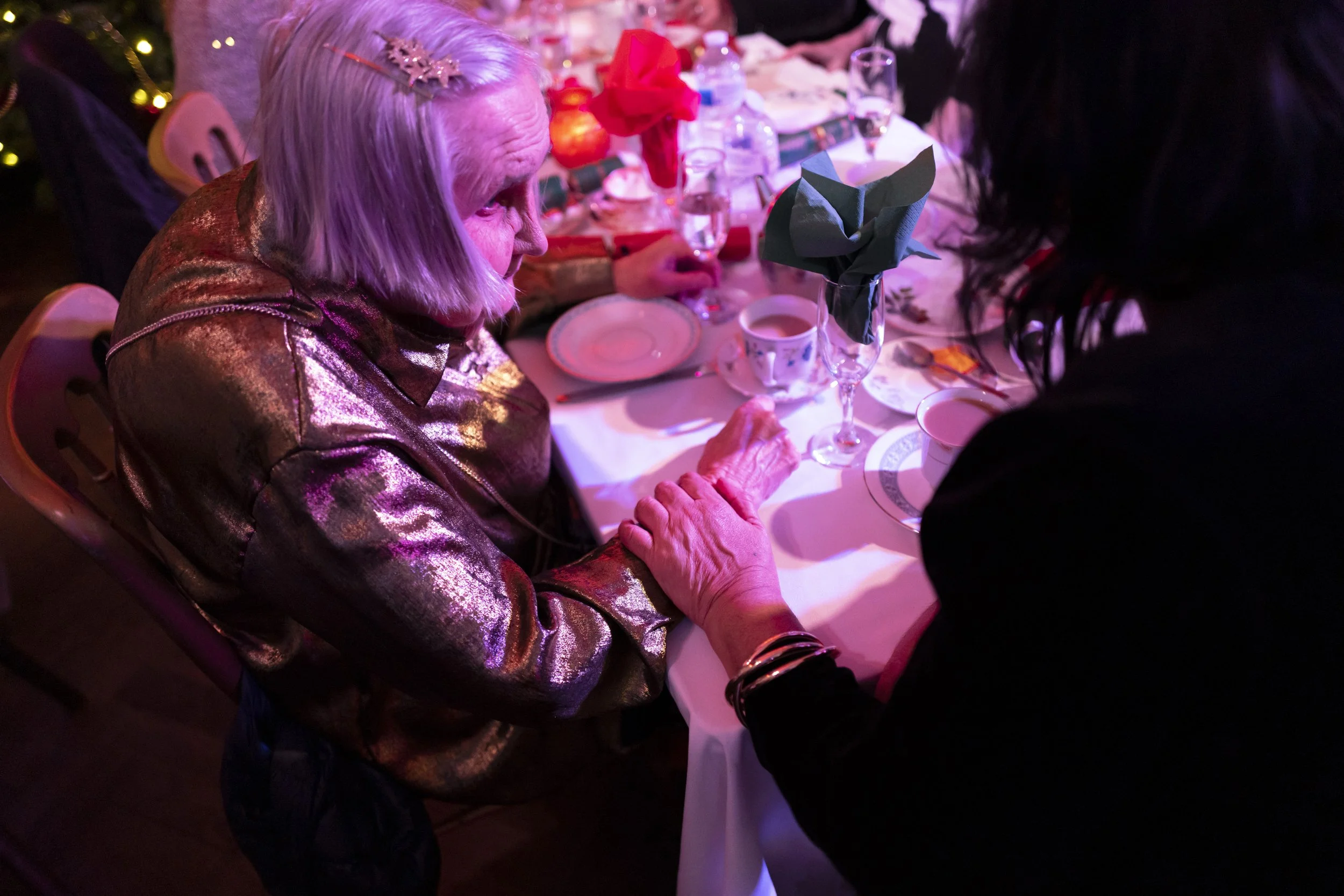  Margarita, a regular attendee, speaks with another guest in a wheelchair at a table during an afternoon at The Posh Club, a social club that brings older adults together for tea, conversation and live entertainment. 