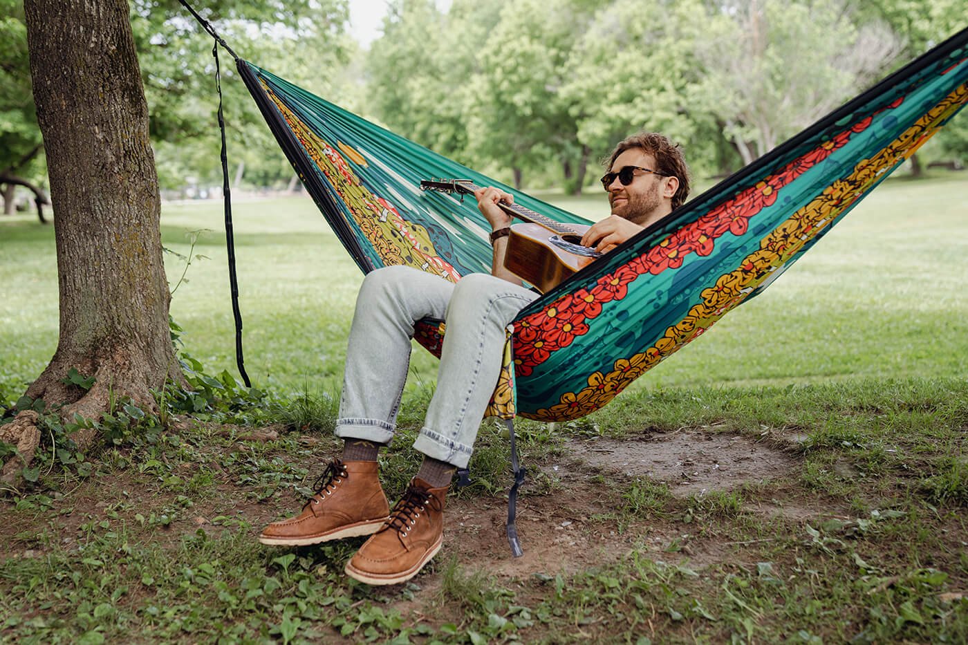  Artist, Logan Hall, plays his guitar in the ENO DoubleNest Hammock Print he designed, Day to Night, in June of 2024. This design celebrate’s ENO’s 25th anniversary.  