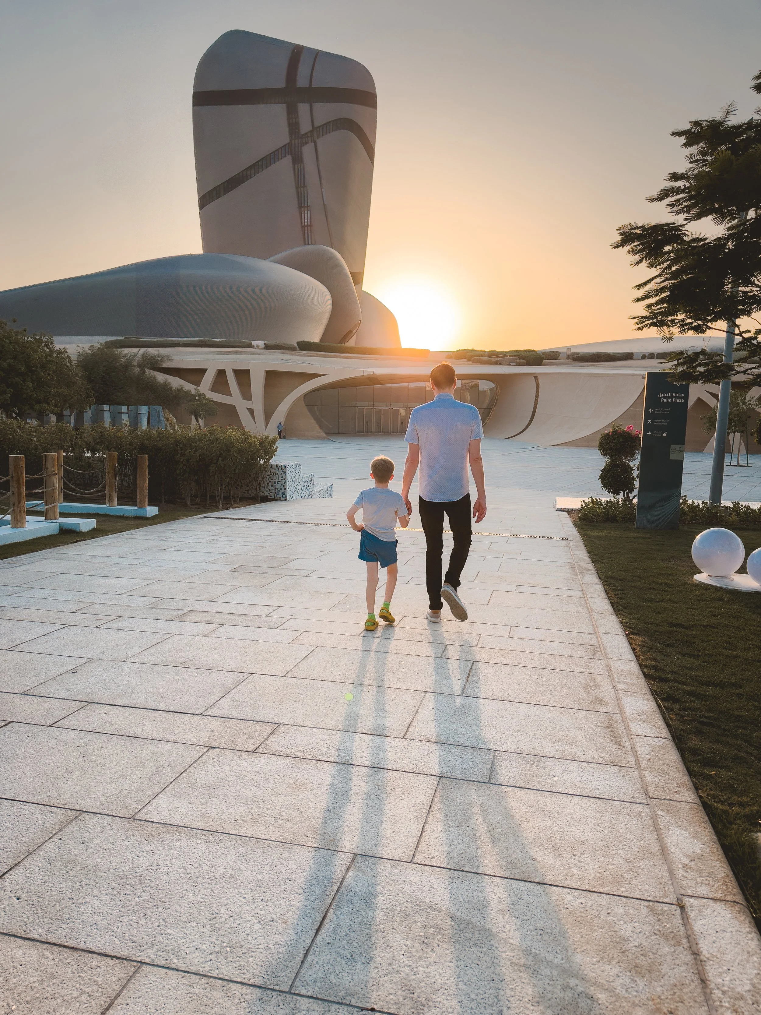 Father and son walking hand-in-hand to Ithra Museum in Saudi Arabia at sunset.