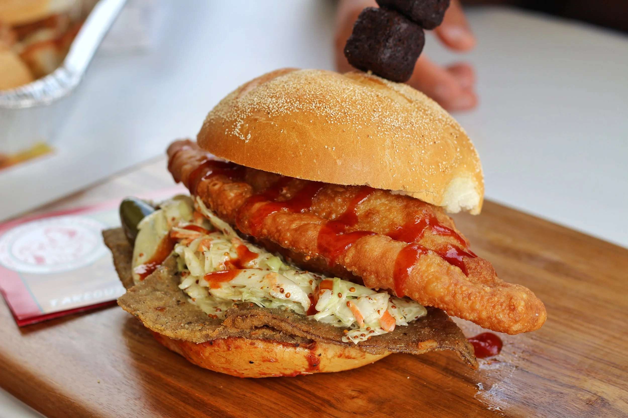 Breaded veal and a pulled pork panzerotti on a Kaiser bun with sweet BBQ sauce, creamy slaw and jalapenos, topped with two deep fried brownies.