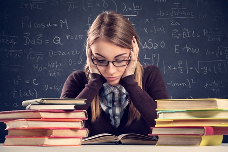 46062516 - young student with desperate expression sitting at a desk and looking at her books