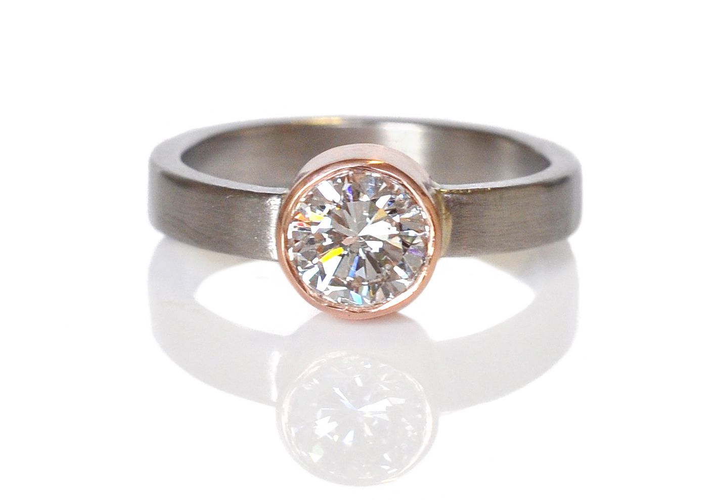 Kristy and Matt brought in this blindingly bright brilliant cut Moissanite stone and designed a sleek and simple setting with a little extra width on the band for a pinch of toughness. 14k red gold bezel set into a wide 950 palladium band.