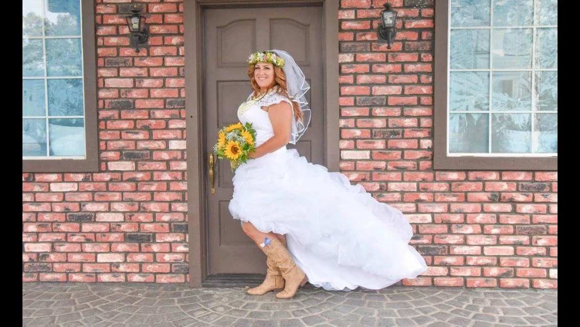  This is a high low gown that looks perfect with her boots! &nbsp;The bodice is hand beaded with a corset back.&nbsp;&nbsp;She is wearing a short 3 tired,&nbsp;tulle veil with a satin edge. It blends well with the ruffling on the skirt.  photo by Amb