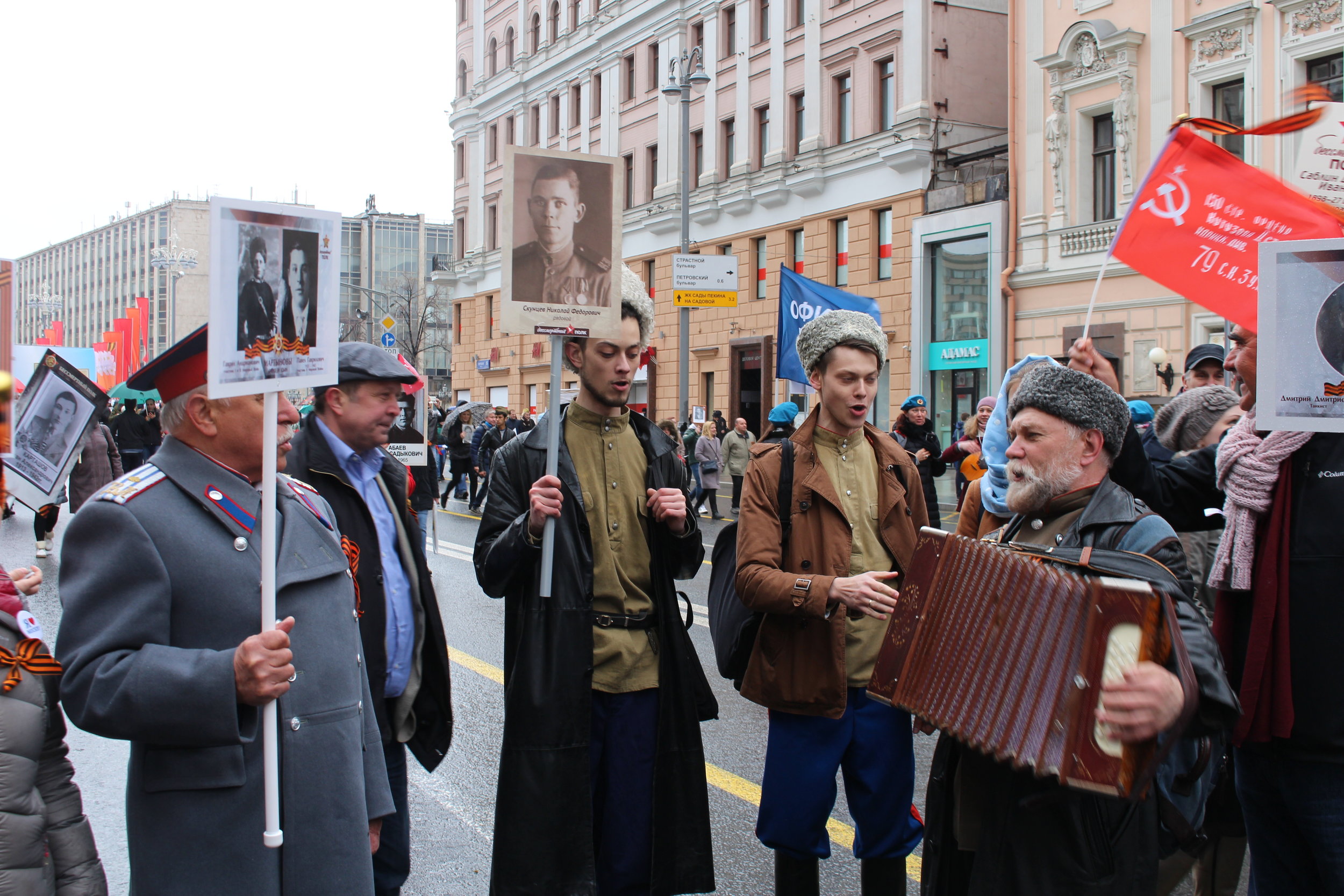 Old and young gather to sing, holding placards to commemorate their ancestors