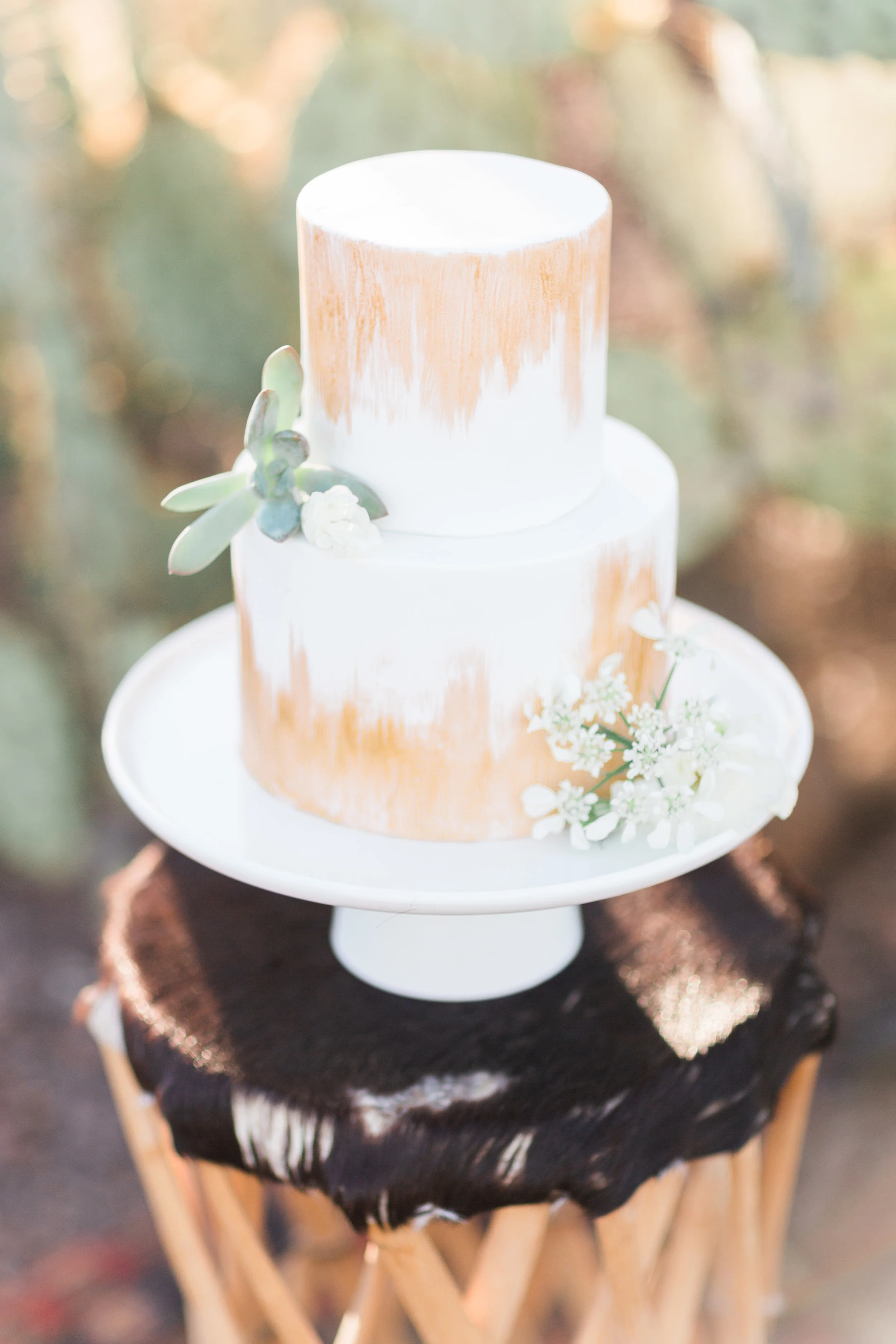 Beautiful white and gold two tiered cake with cactus in the background