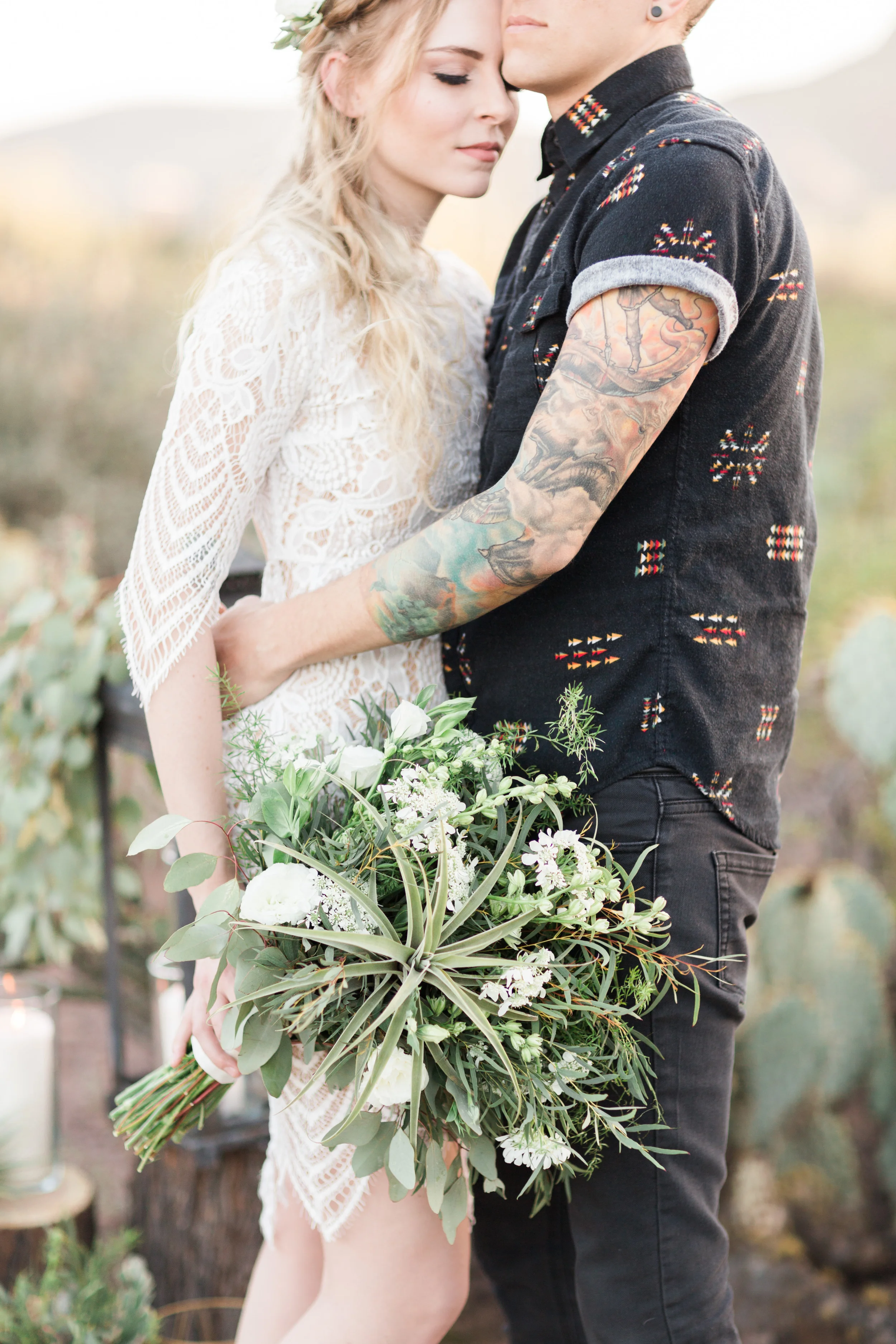 hipster groom hugging his bride who is holding a gorgeous green and white bouquet