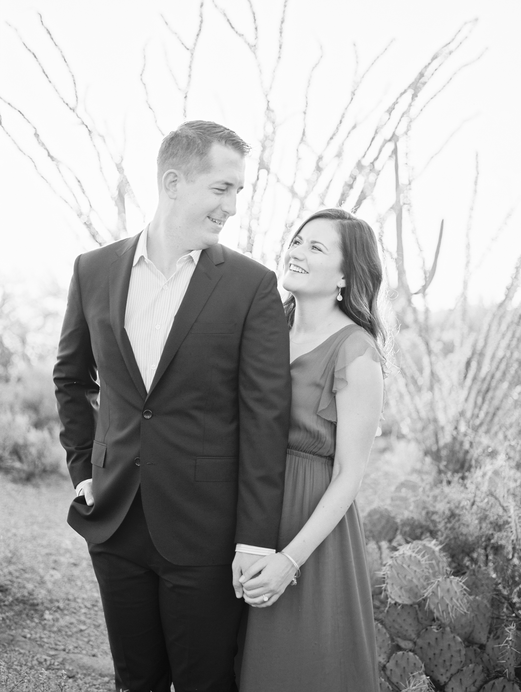 Bride & groom to be smiling at each other at their desert engagement session.