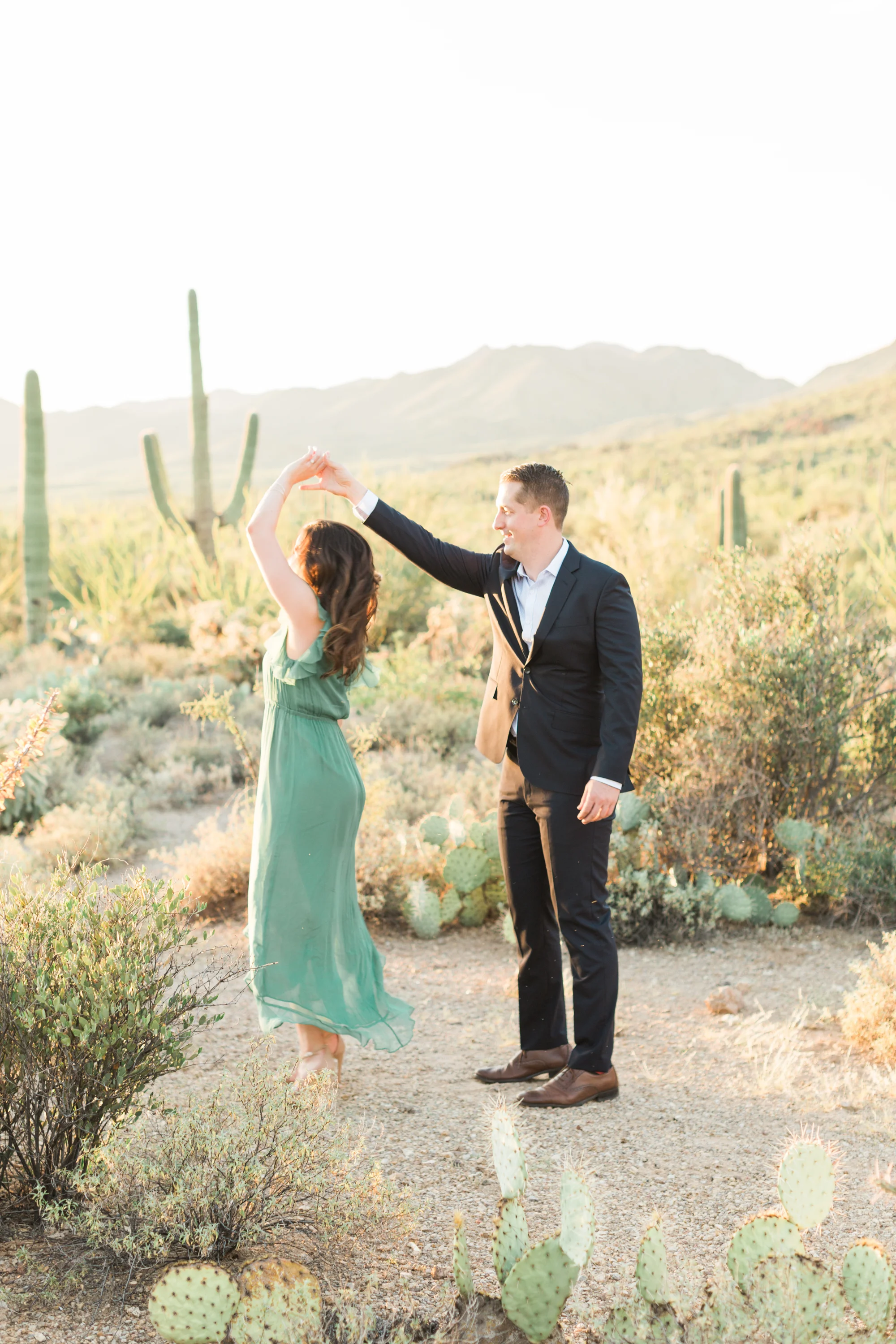 Cute couple dancing in the desert at their Tucson engagement session. Gorgeous desert light and cactus glowing in the background.