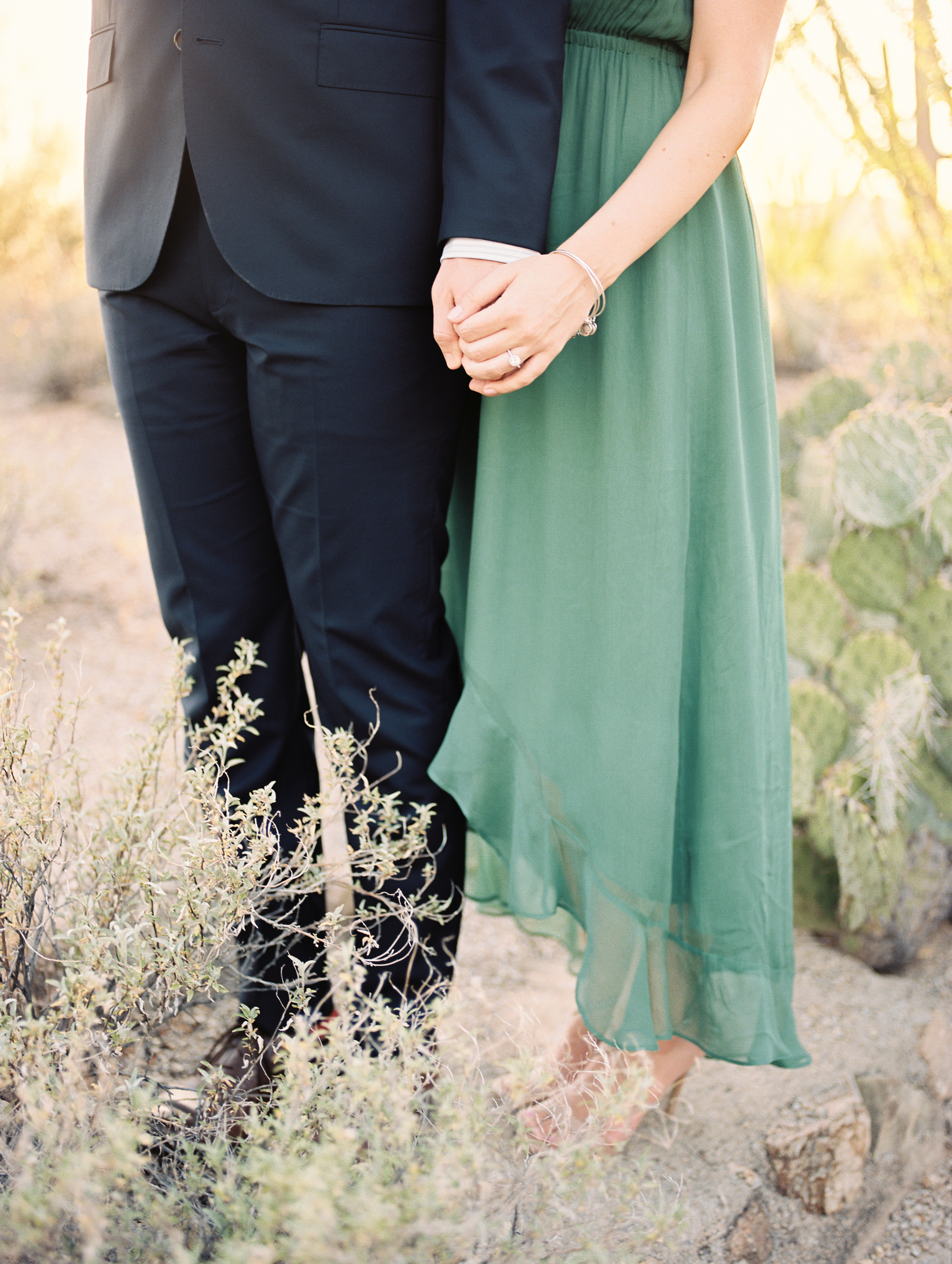 Couple holding hands in the desert at their Tucson engagement session. Gorgeous greens and beautiful engagement ring.