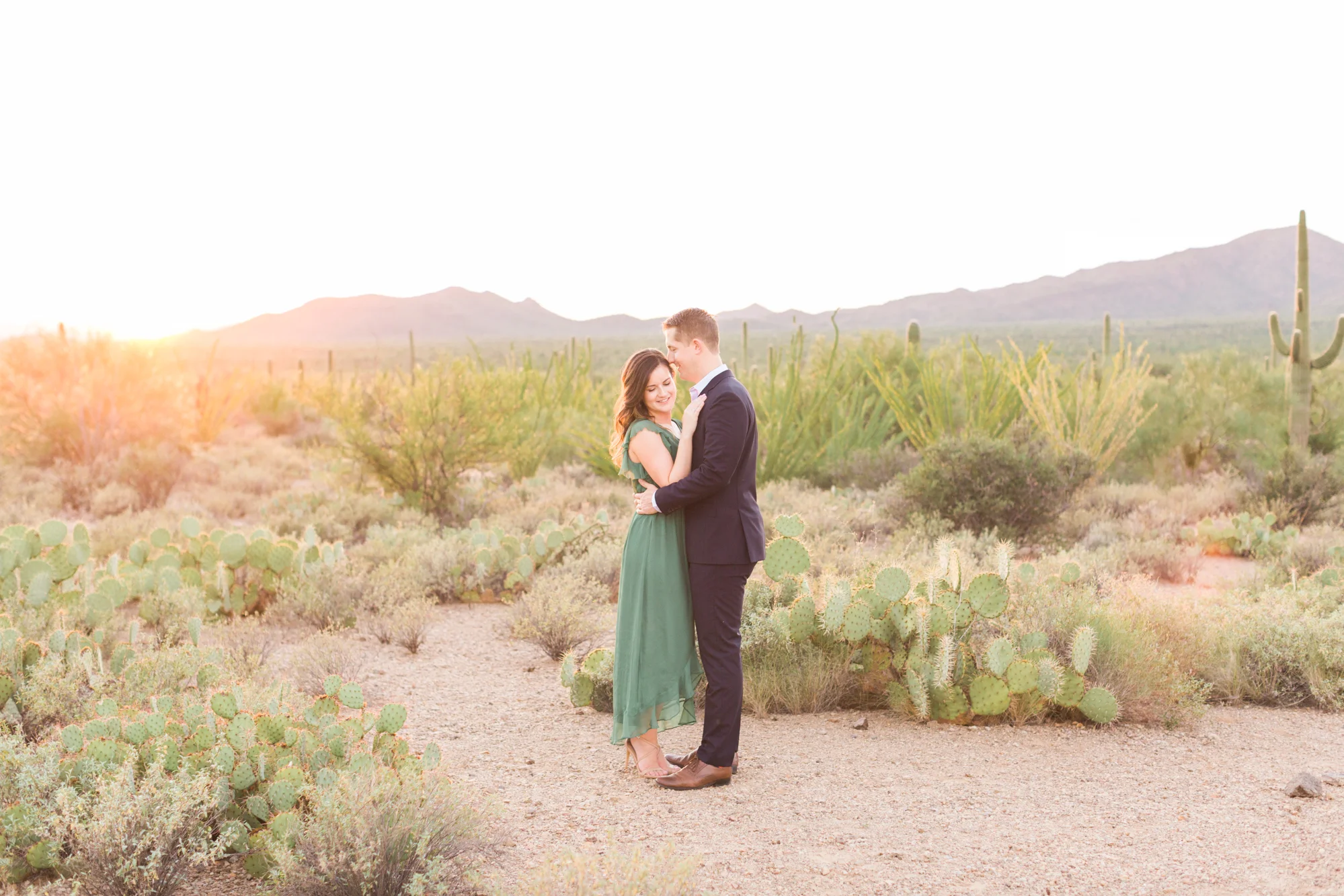 Engagement photo of an adorable couple hugging each other with the Tucson sunset and gorgeous desert in the background at golden hour. 