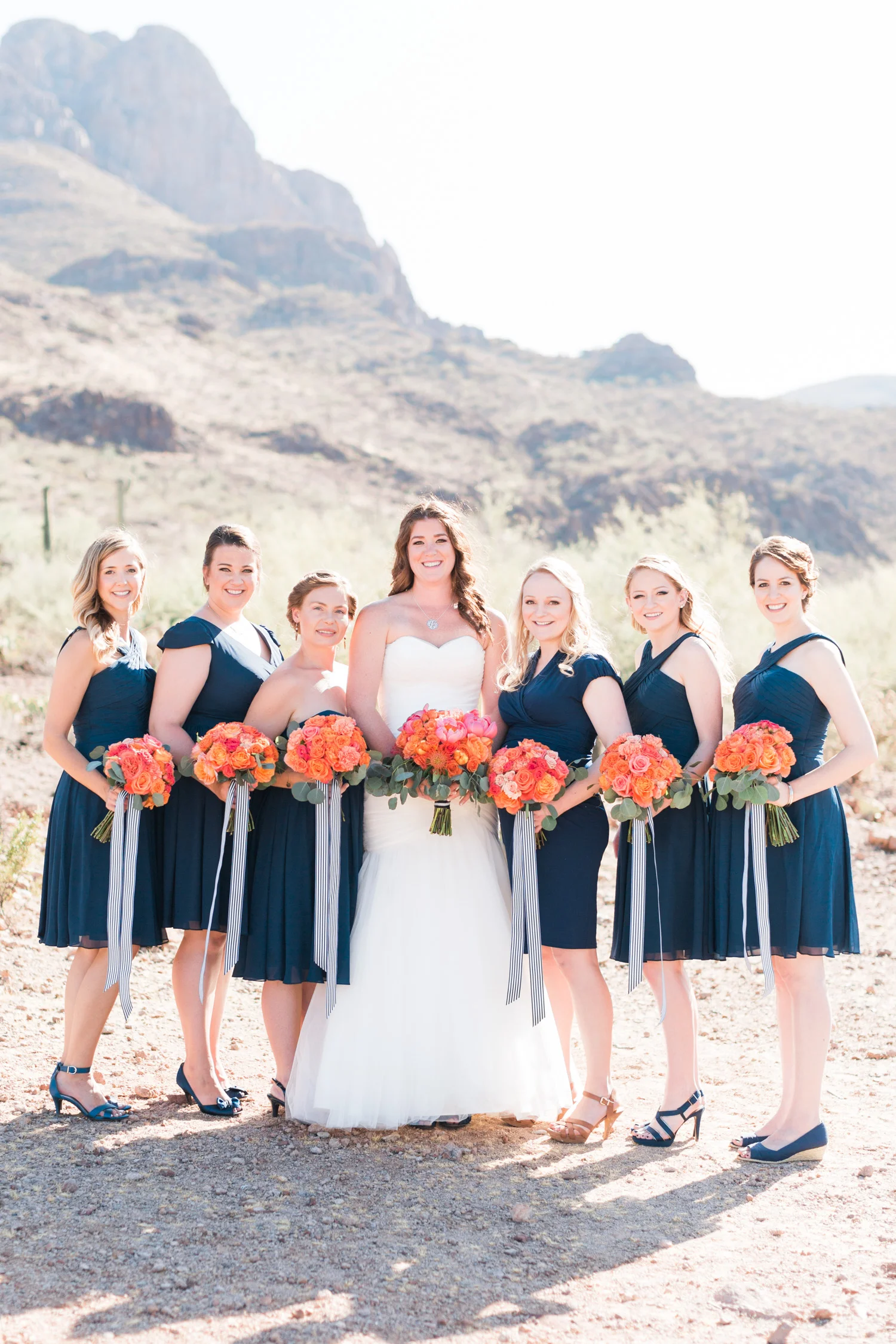 Beautiful bride and bridesmaids in navy with salmon bouquets, smiling at the camera.