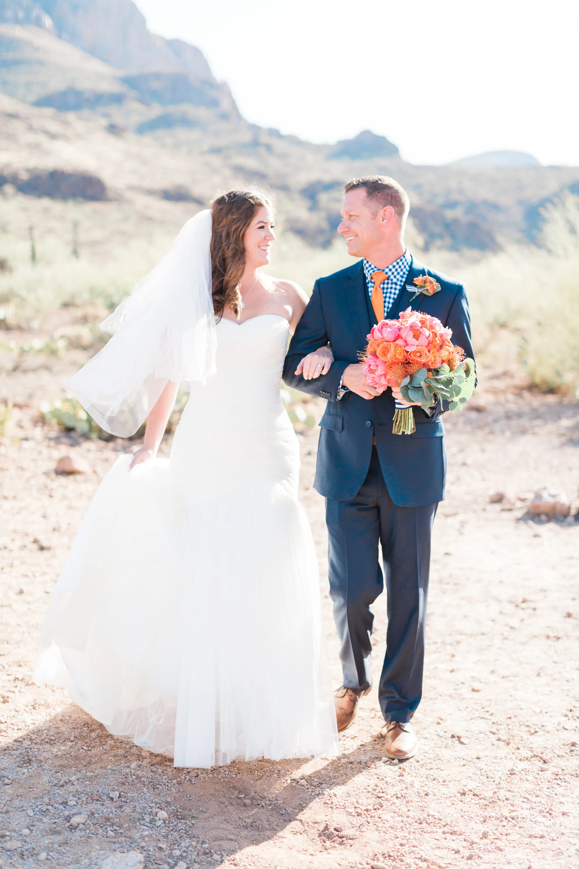 Bride and groom walking towards the camera. Groom holding bouquet and bride holding her dress. Love the light and airy feel of this beautiful Tucson summer wedding. 