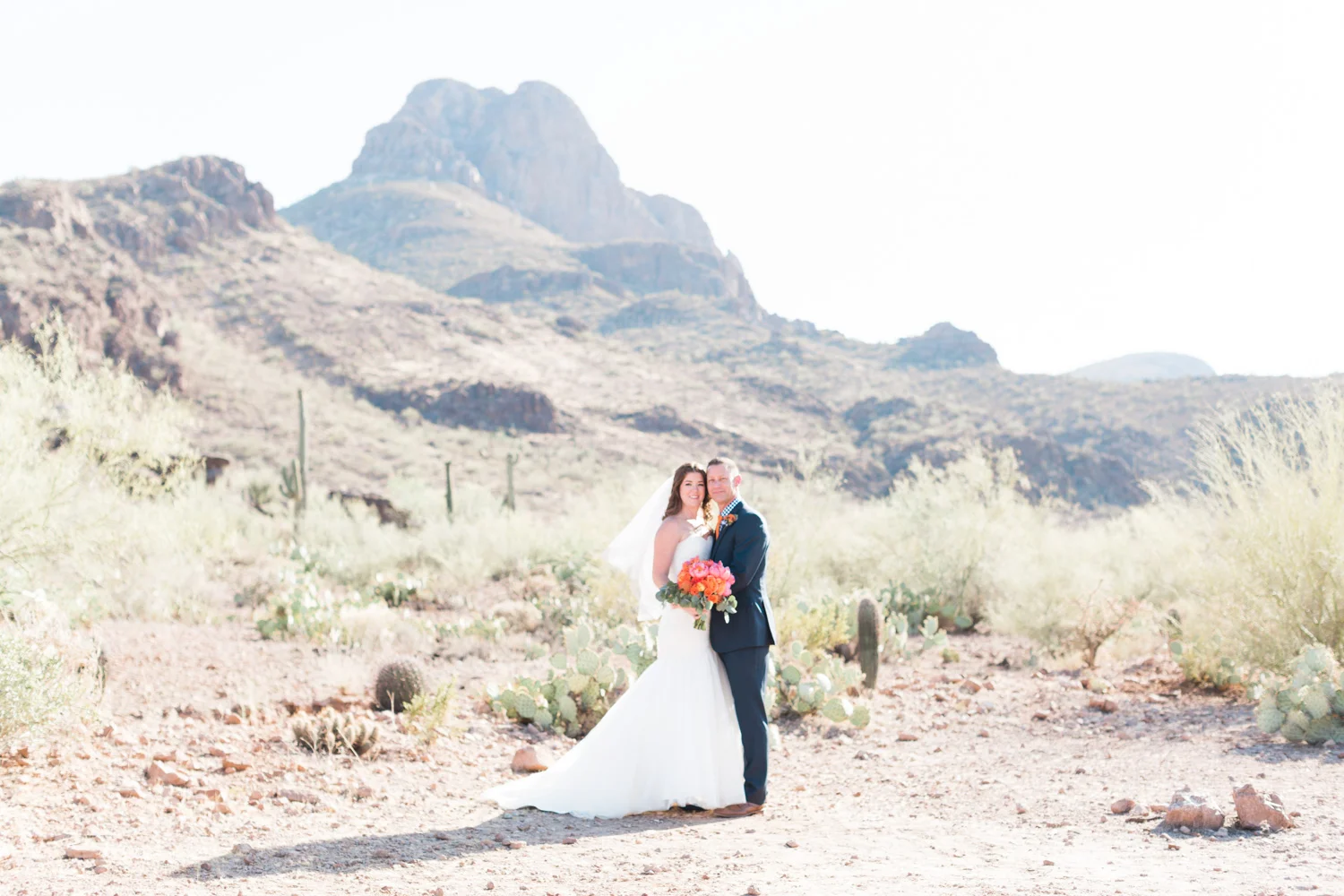 Bride and groom standing in a gorgeous desert setting. Love those stunning mountain views an the cactus in the background! Perfect desert wedding venue.