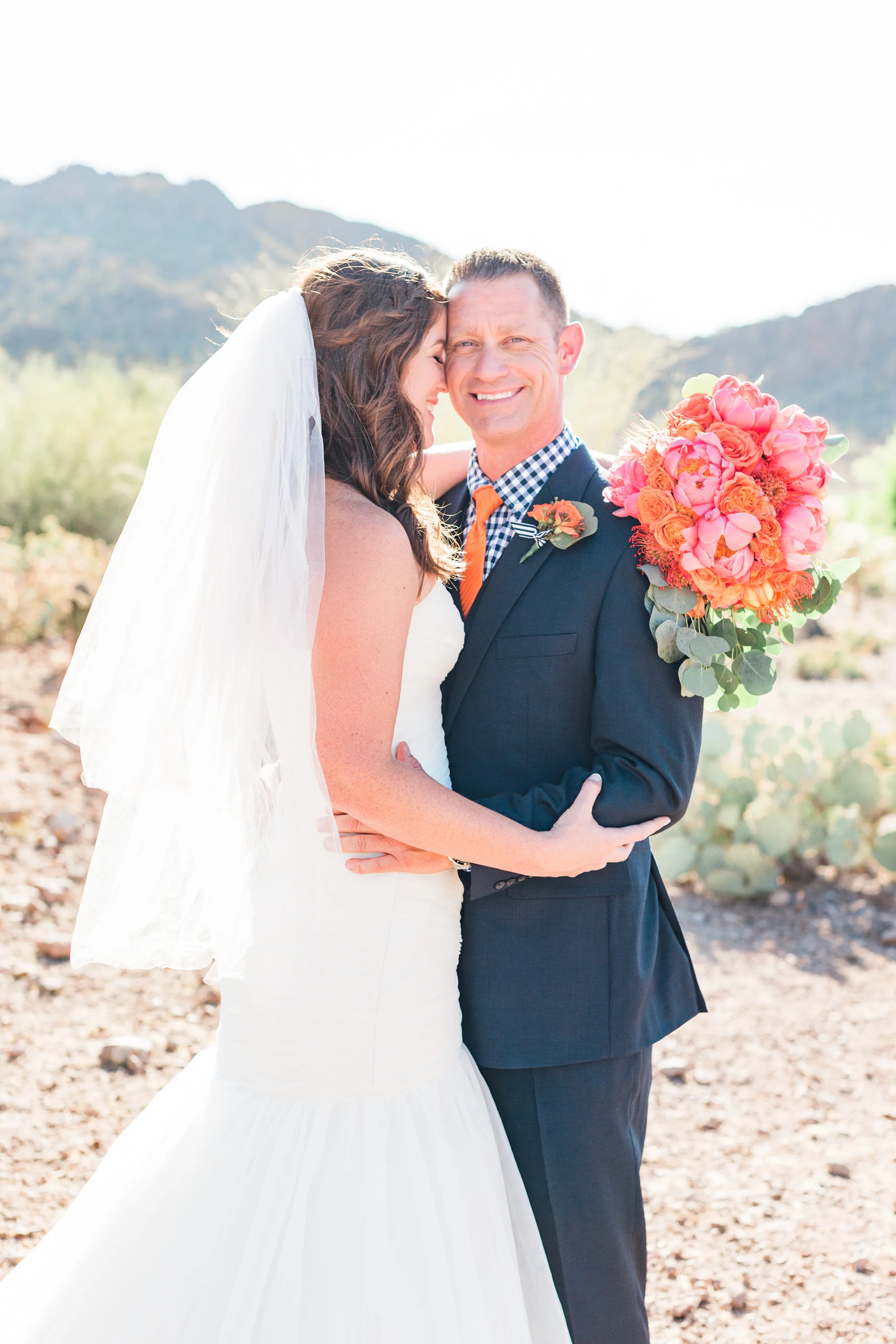 Bride hugging her groom, who is smiling at the camera. Love that beautiful desert light shining from behind them! 