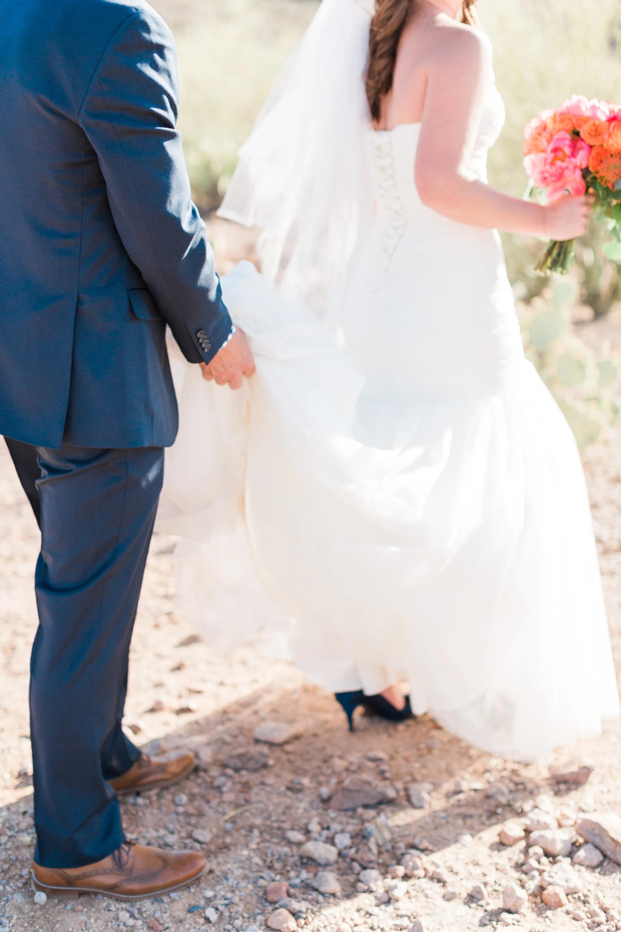 Groom carrying his brides dress as she treks through the rocky Tucson desert in heels.