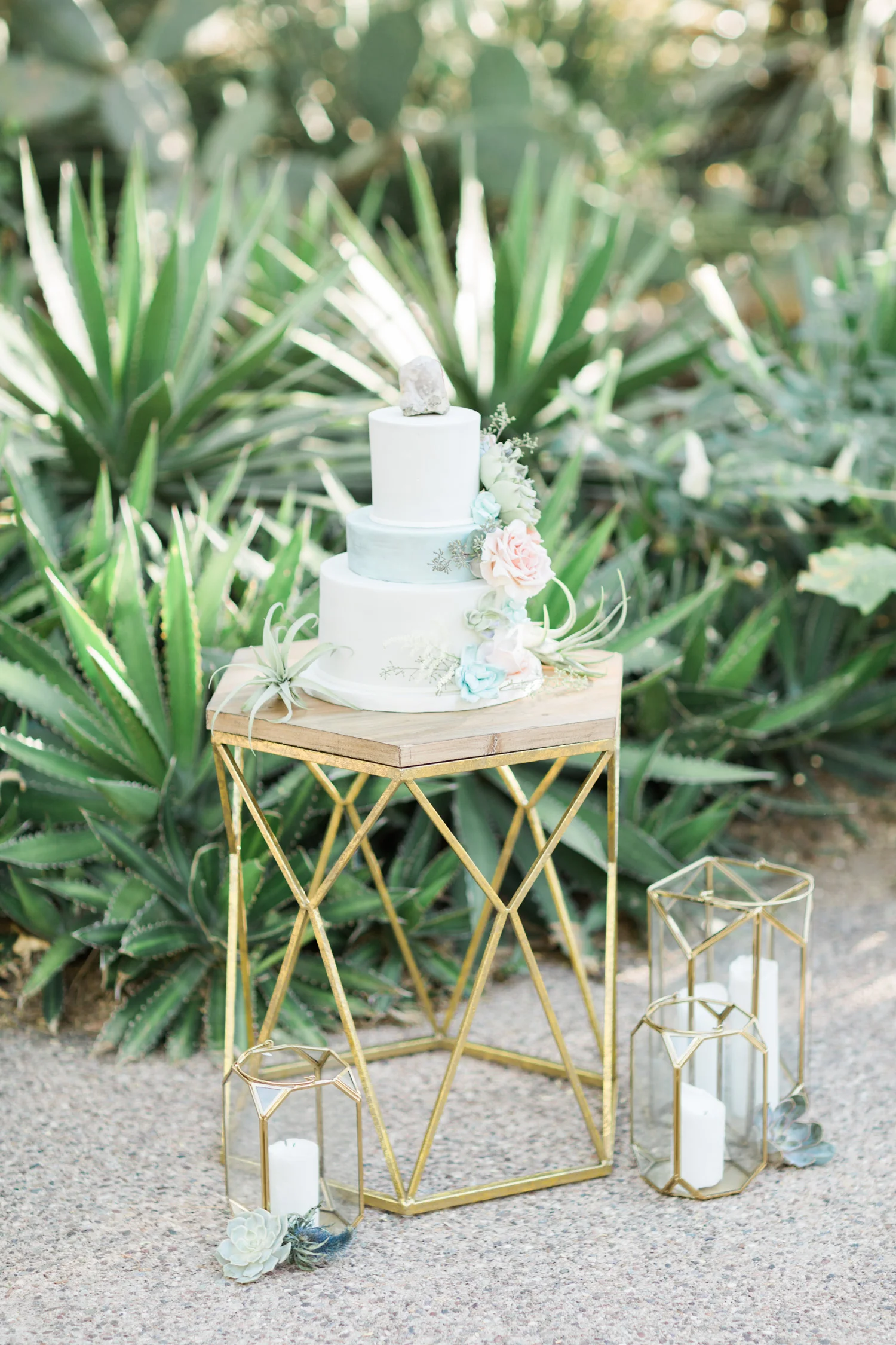 Stunning hand crafted wedding cake on a gold geometric stand, surrounded by gold lanterns