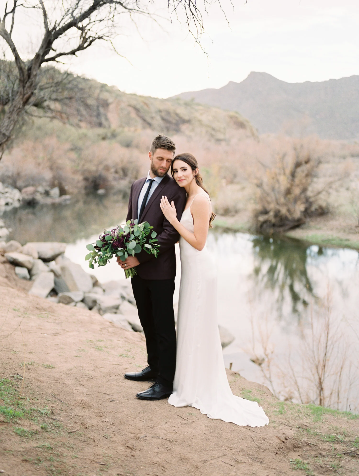 Gorgeous bride embracing her groom who is holding her bouquet. Gorgeous salt river views in the background.