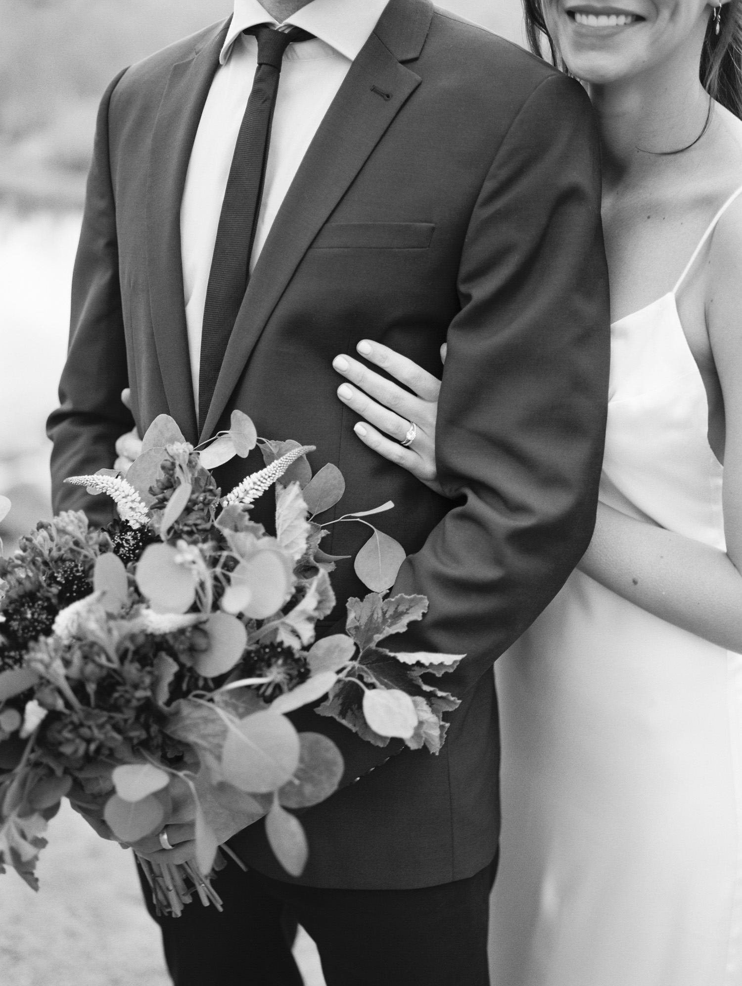 Black and white photo of groom holding bouquet and bride smiling and hugging her groom.