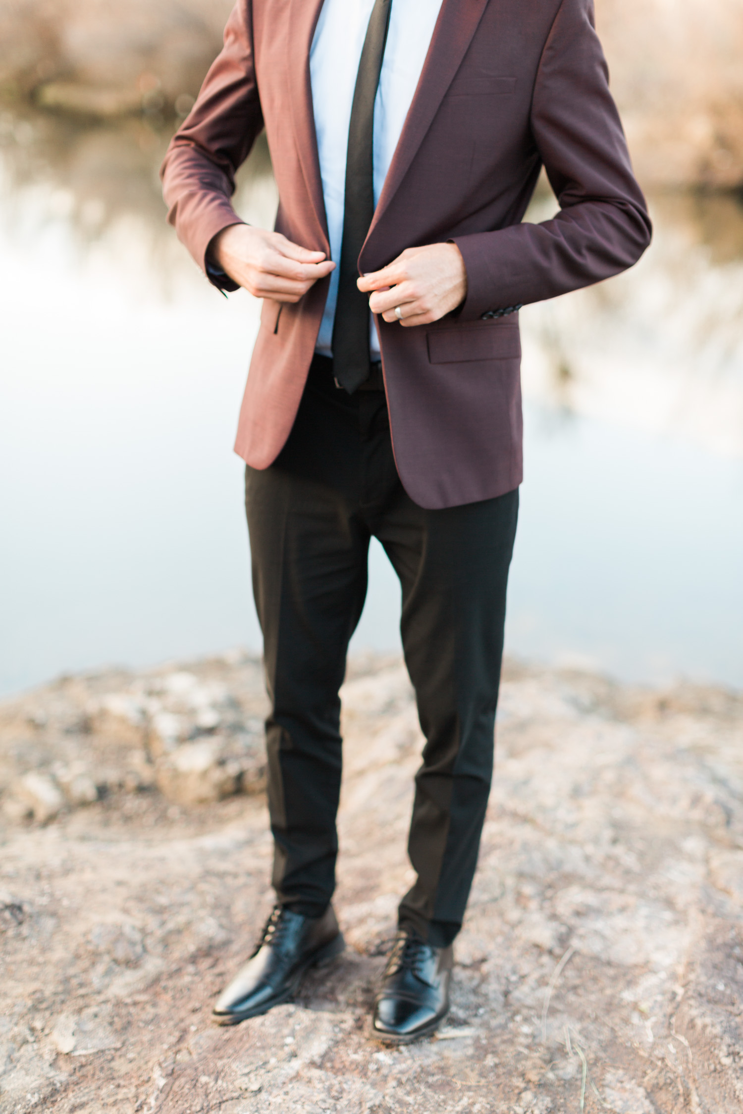 Groom buttoning his burgundy jacket on his wedding day.