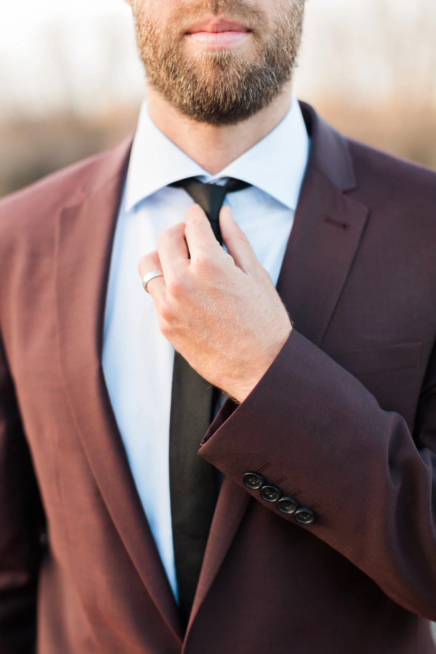 Straightening his tie, wearing a classy burgundy jacket.
