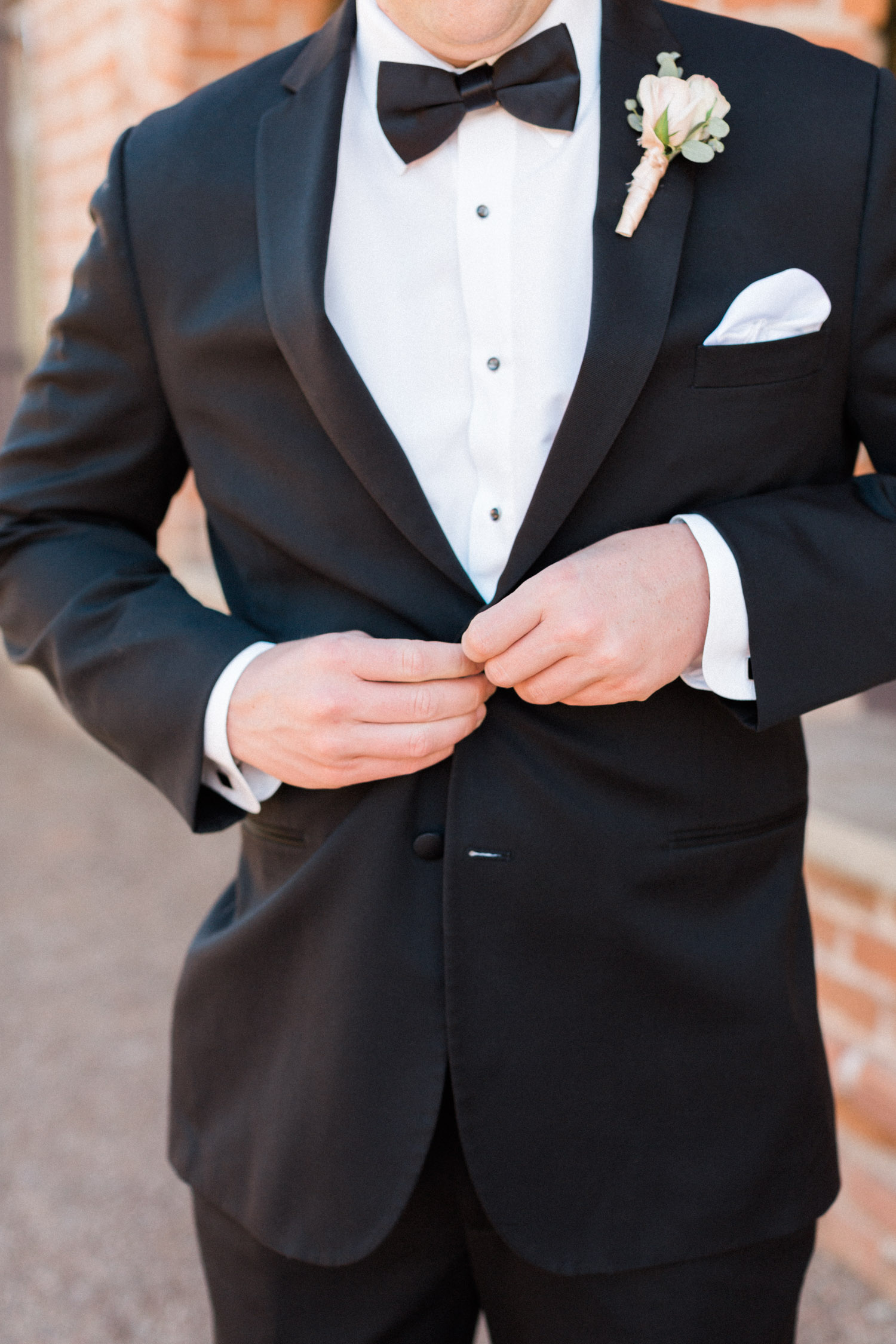 Groom buttoning up black tuxedo