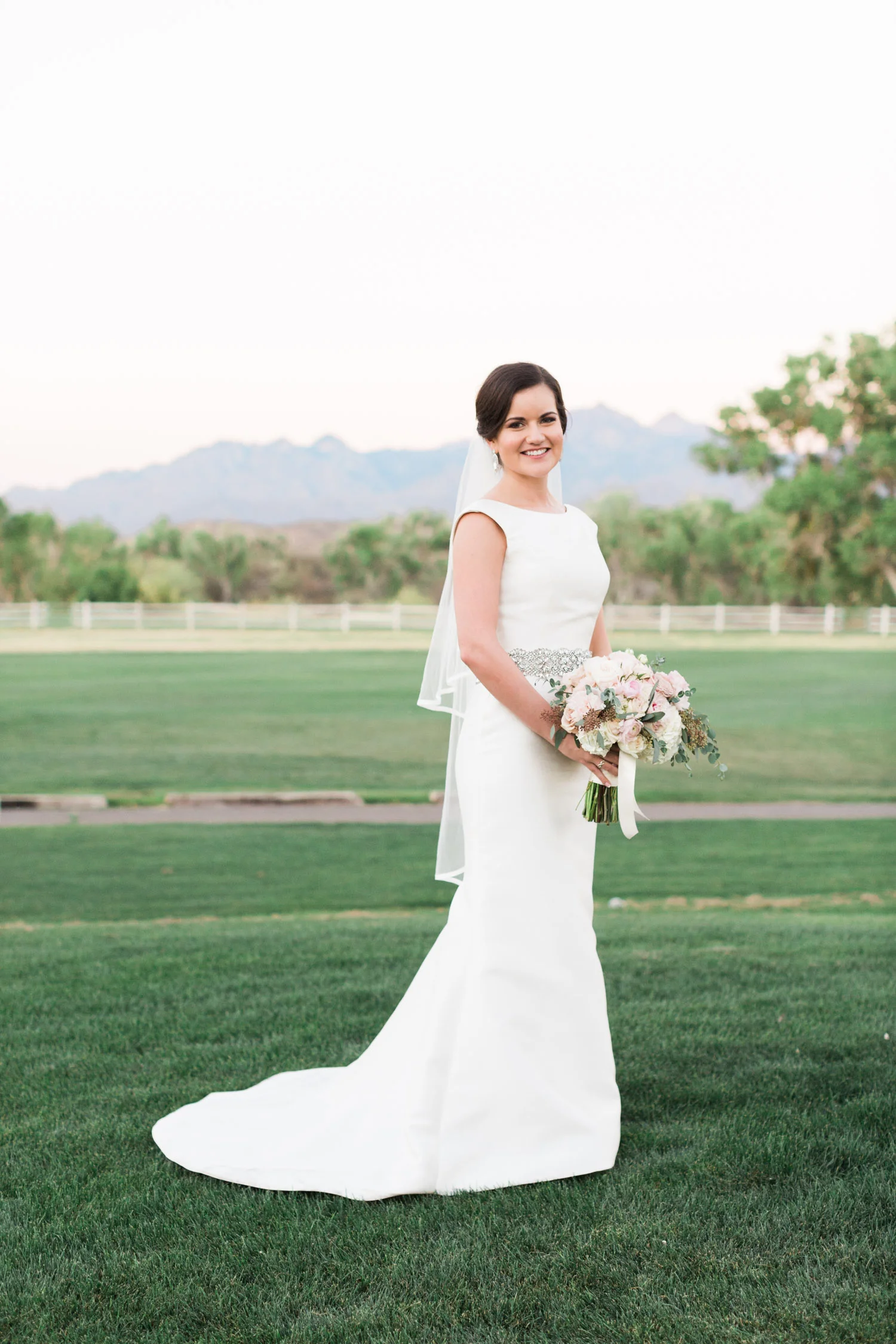 Bride wearing a fitted Pronovias gown, holding flowers with mountain views in the background 