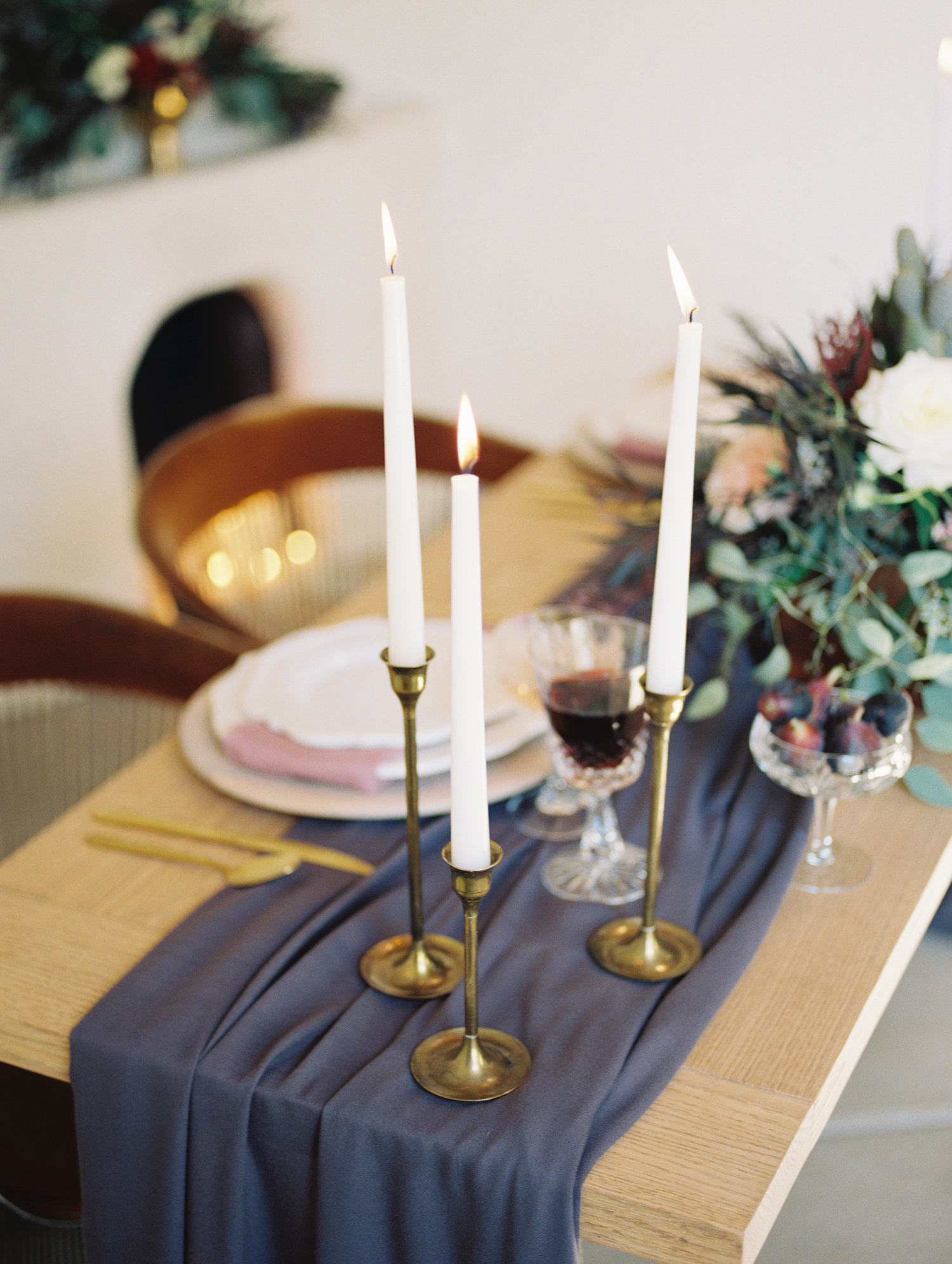 table setting with tall white tapered candles in brass candlesticks and a plum table runner 